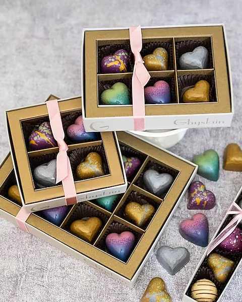 Ghyslain's Box of Hearts - Indulge your senses with our seasonal chocolate collection, featuring Ghyslain’s imaginative, hand-painted chocolate shells filled with rich ganache infused with exotic flavors sourced from the finest ingredients. Our 4-12 count signature window boxes with metallic gold surround beautifully presents an assortment of delectable gourmet chocolates from Ghyslain’s limited release Valentine Collection. Flavor selections are randomly chosen.  All prices in USD ($)