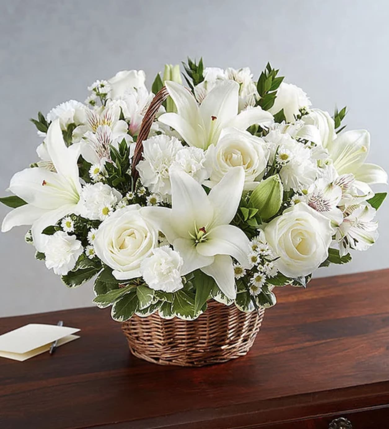 White Wishes - Express your deepest condolences with this elegant sympathy basket. Delicate white lilies and carnations create a serene and comforting display, offering solace during a time of loss.