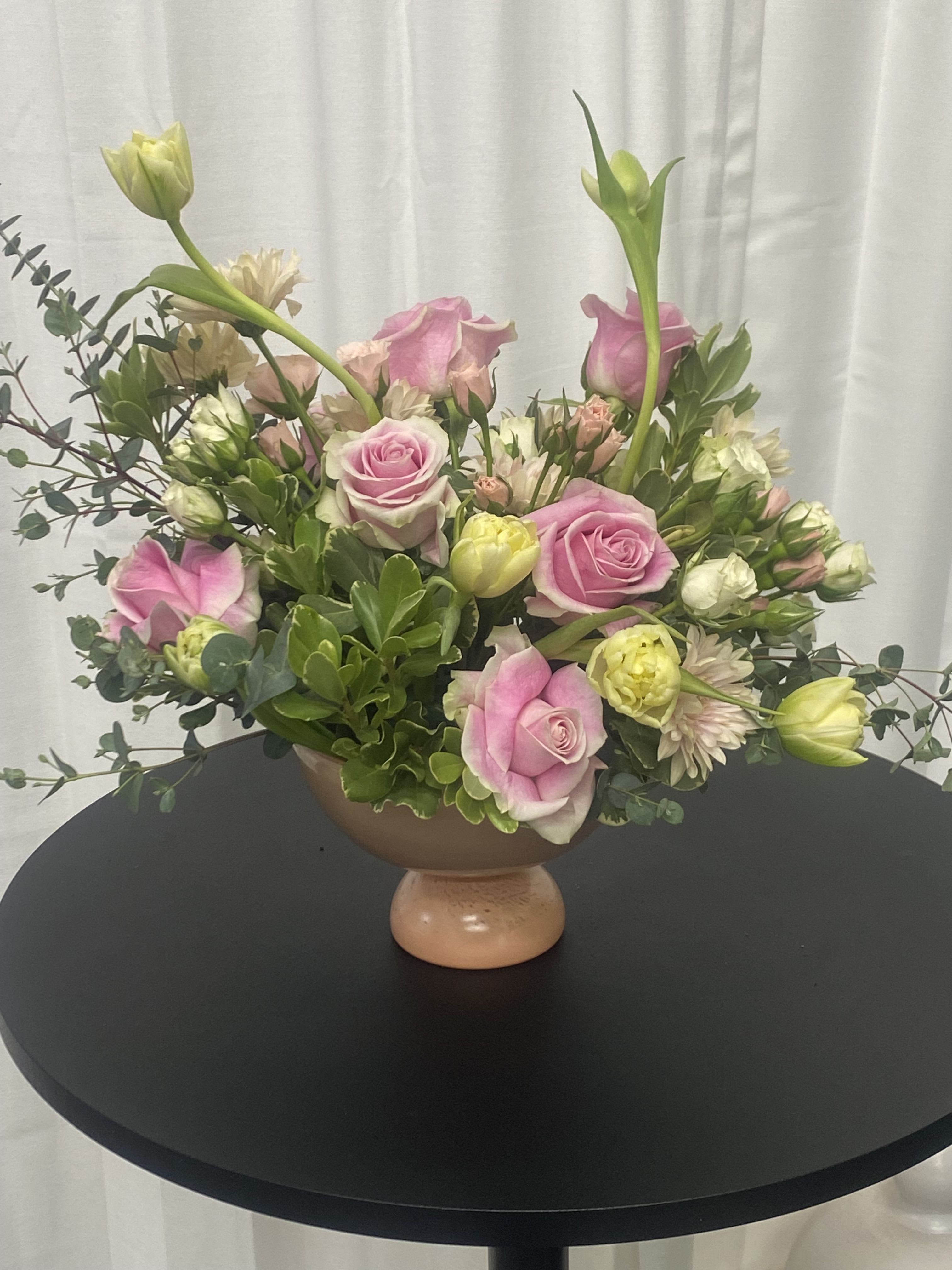 Pretty and Pink Pretty and Pink - Creamy dancing tulips, regular pink roses, miniature pink and white roses, ample greenery, pittosporum, salal, and eucalyptus. This beautiful foliage is arranged in a soft pink pedestal dish and kissed with love