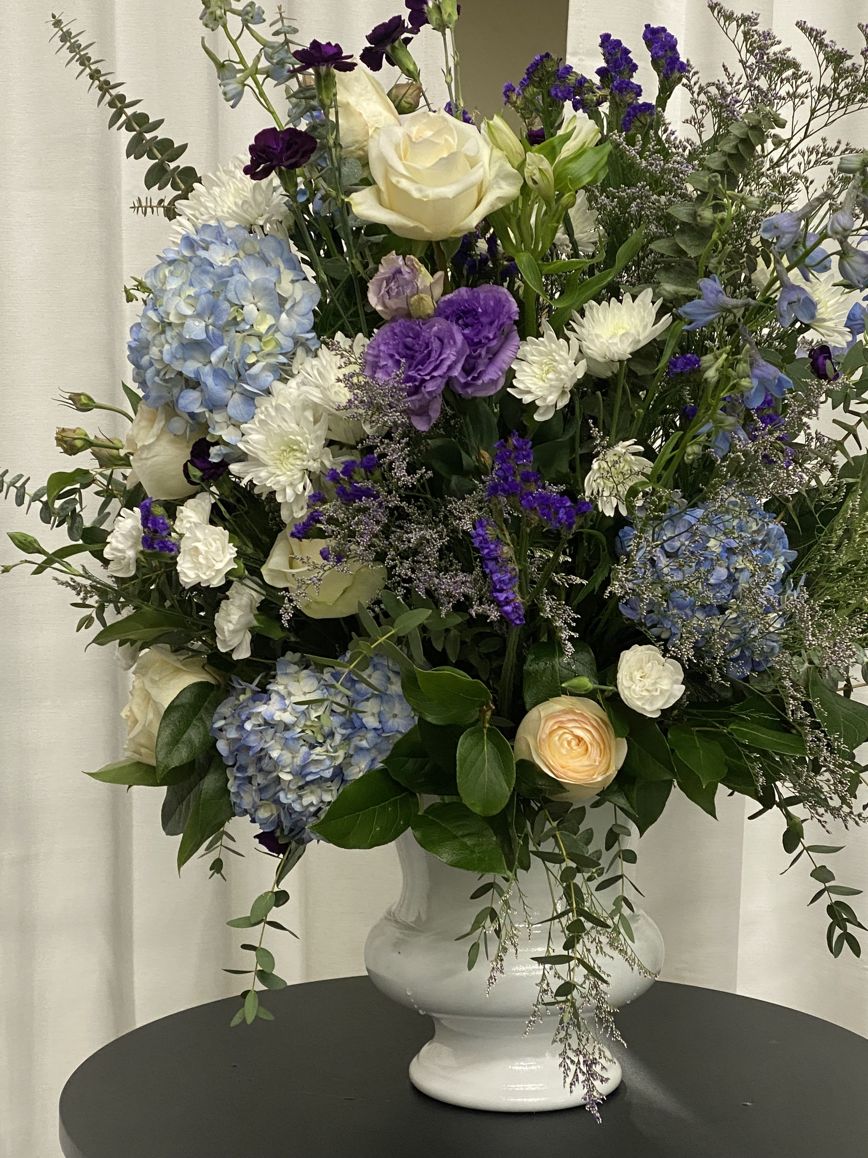 Praising Purple Praising Purple - A large funeral arrangement is dressed in purple for that royal, regal, memorial tribute. Purple lisanthanus, blue hydrangeas, white roses, white disbuds, white miniature carnations, and other greens filled to value