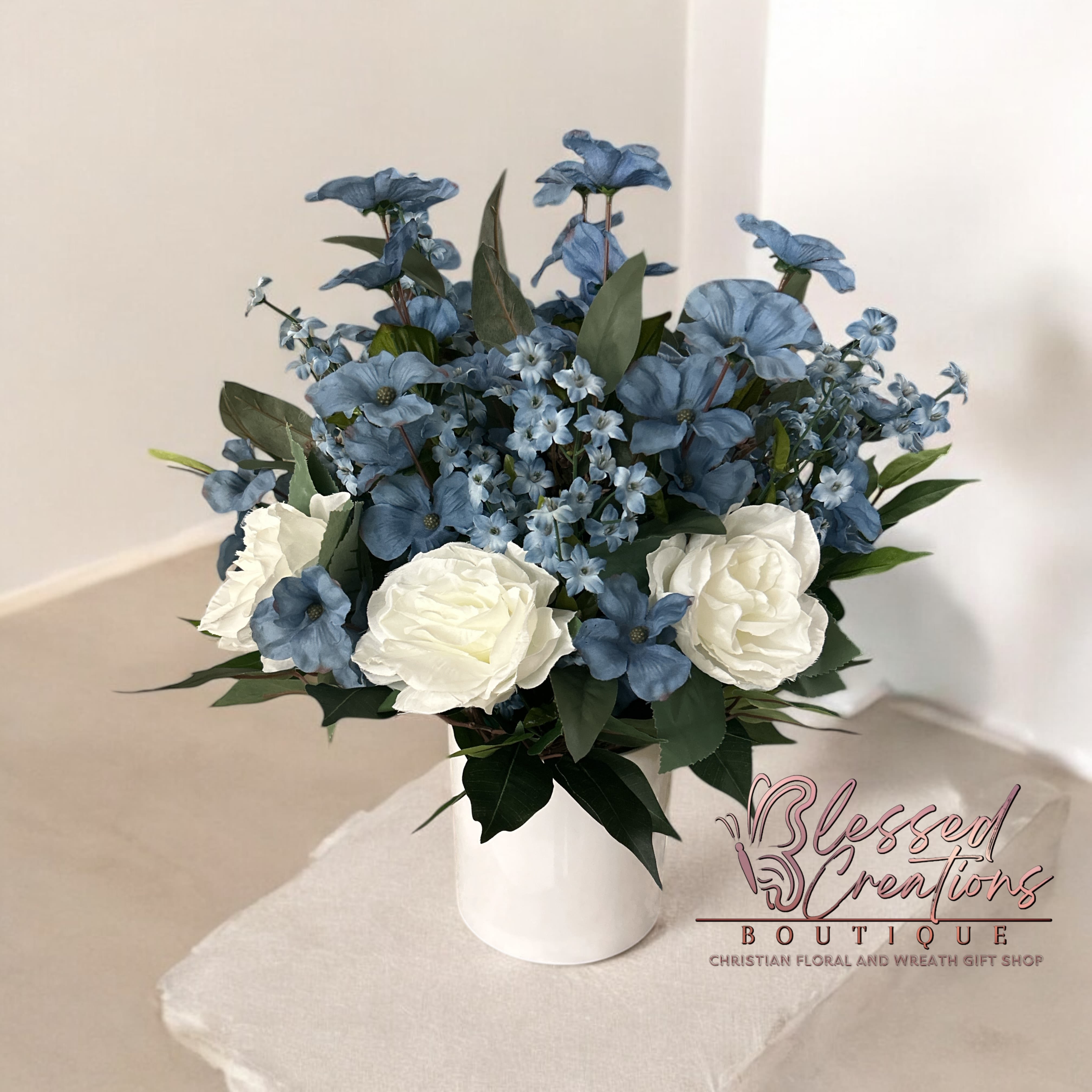 Dusty blue and ivory silk arrangement Dusty blue and ivory silk arrangement - A serene and elegant sympathy arrangement featuring dusty blue and ivory silk florals. This timeless design offers a gentle expression of comfort and remembrance, blending soft hues with delicate textures to honor a loved one with grace and beauty.