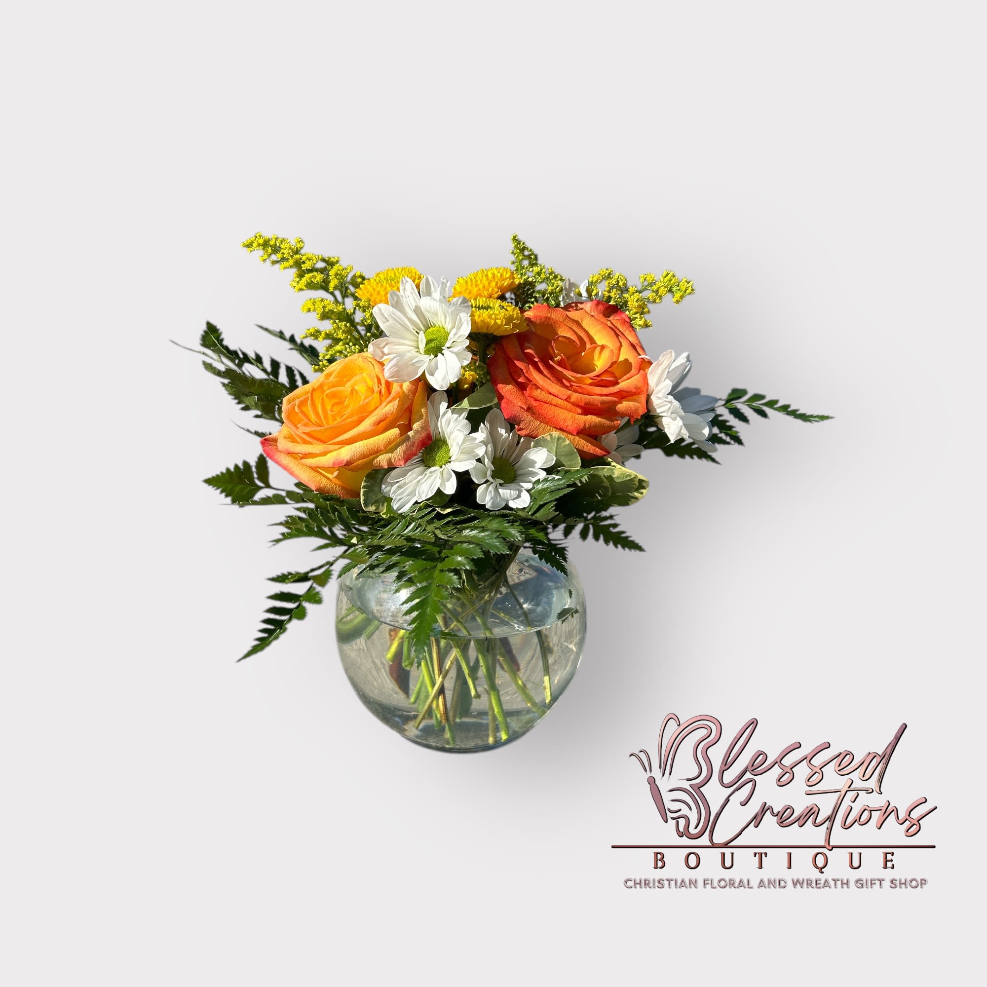 Light of His Love - A vibrant expression of faith and beauty, this uplifting arrangement features radiant orange roses paired with cheerful white daisies, solidago, yellow button mums, nestled among lush pittosporum and delicate fern. A graceful reminder of God’s light, love, and the joy found in His creation.