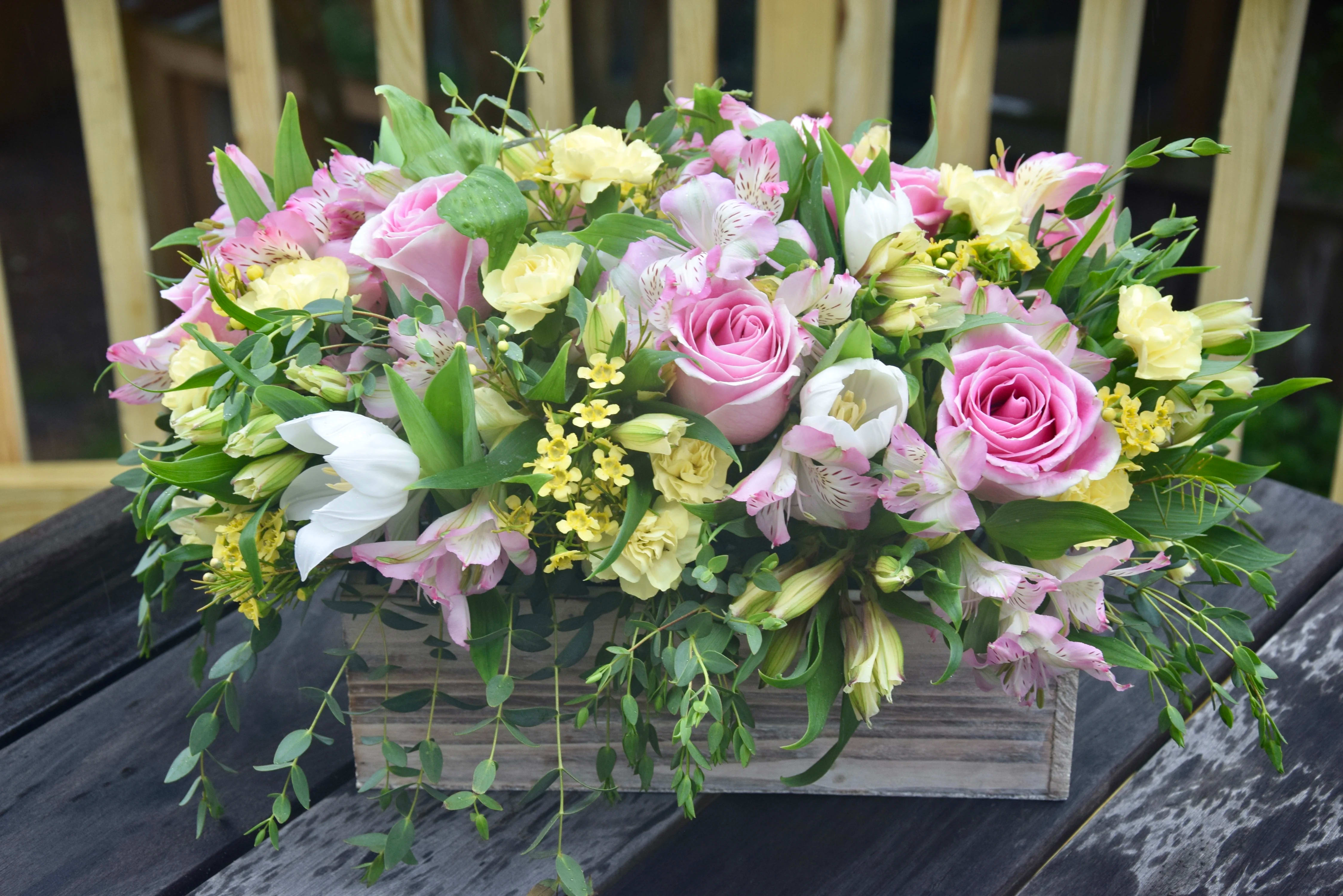 Flower Delight - A lush mix of alstroemerias, tulips, and roses with green fillers in white-yellow-pink color tones, all arranged in a 12inch long wooden planter. A fabulous arrangement to keep or give.