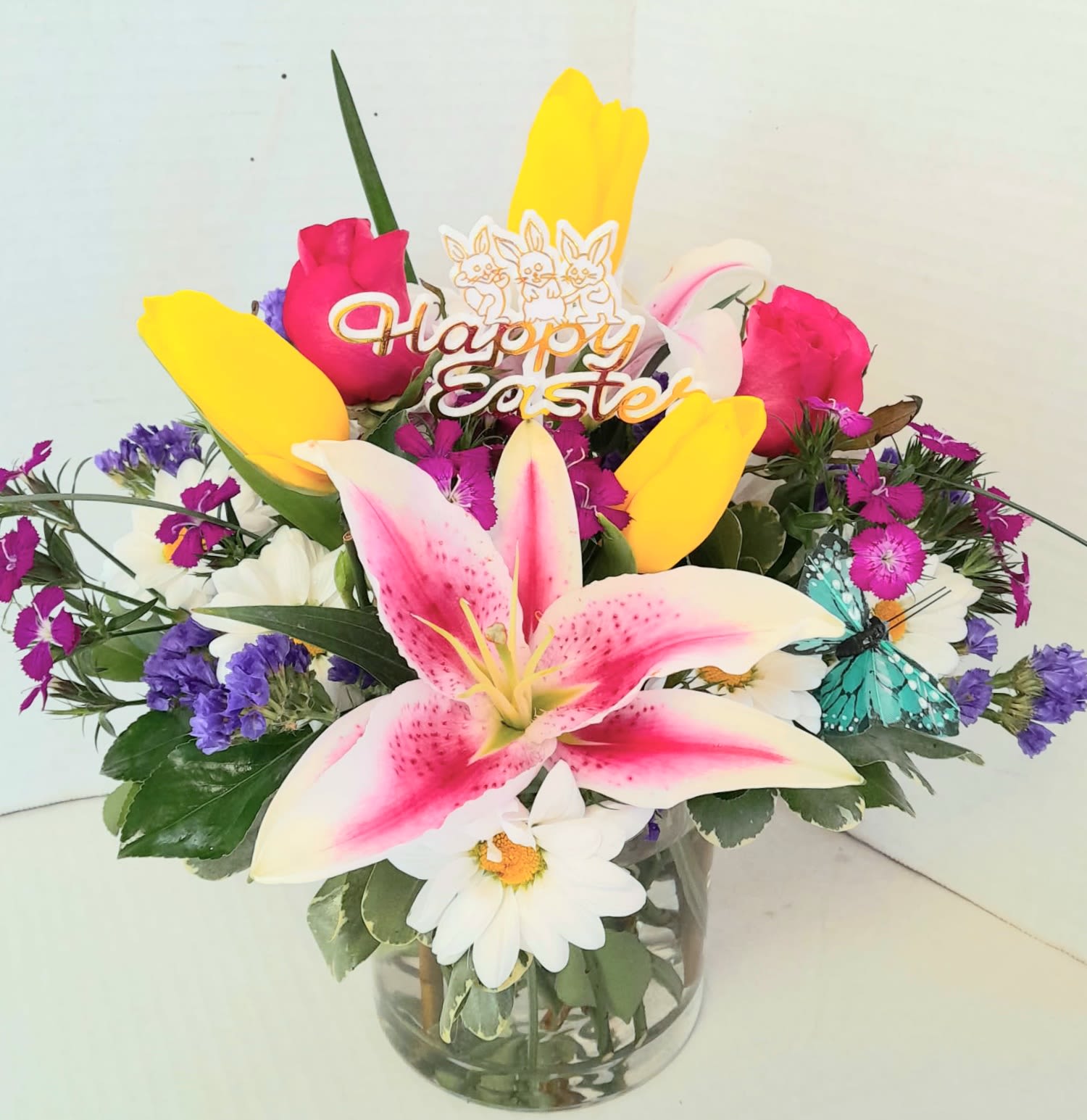 Easter Bowl of Blooms - A colorful mix of roses, tulips, daisies and a stargazer lily with spring accents in a clear cylinder with a butterfly. Perfect for spring and Easter