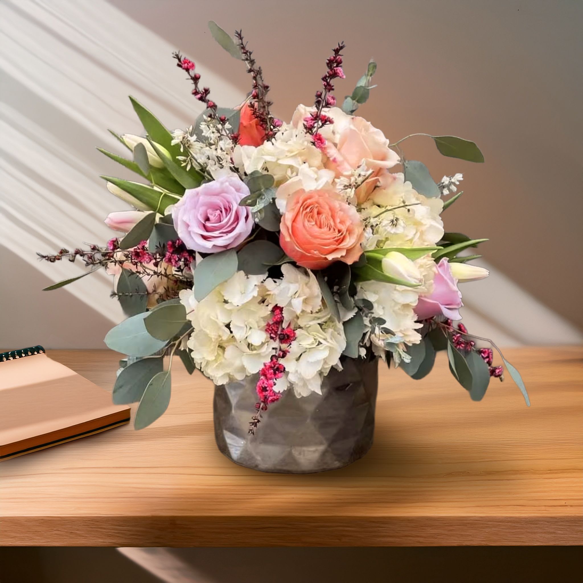 Ariel Design <3 Ariel Design <3 - This romantic, garden-style arrangement features a luxurious blend of Kahala roses in soft peach tones, delicate blush pink roses, crisp white tulips, and white lisianthus, all accented with trailing eucalyptus greenery for an organic, airy feel. The soft pastel palette is both elegant and inviting, making this design ideal for celebrations, heartfelt gestures, or everyday luxury. Arranged in a clear glass vase, the blooms are showcased in a fresh and modern silhouette that enhances their natural beauty.