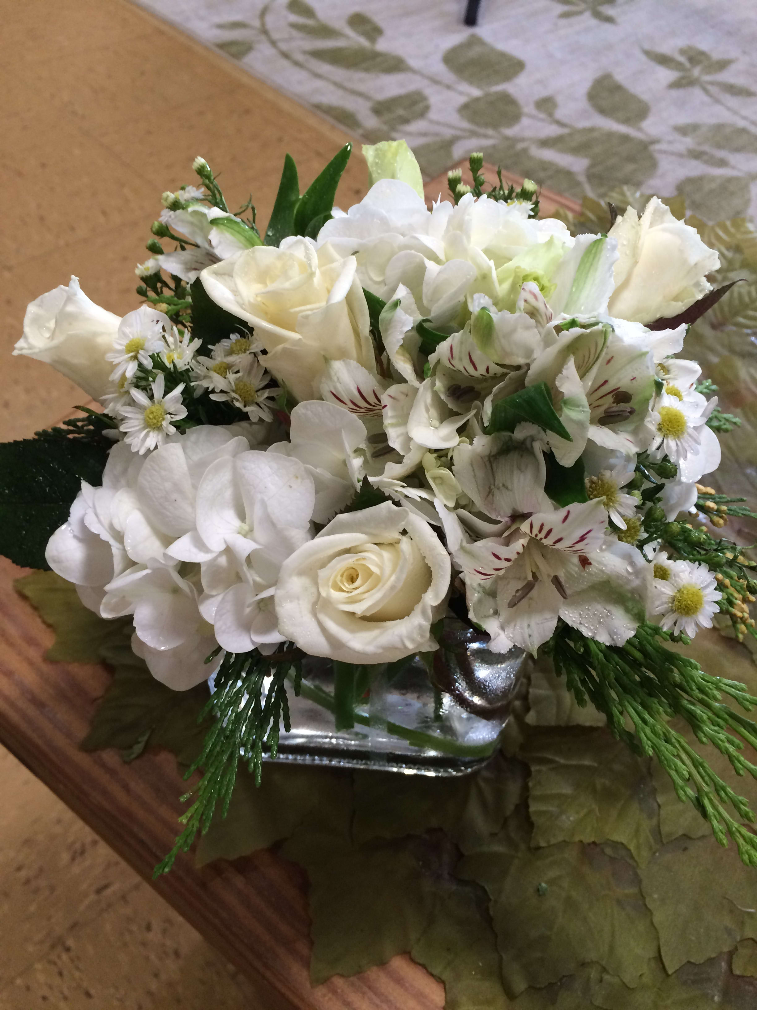 Winter White - A holiday arrangement, with winter greens and white flowers, including roses, hydrangeas and alstromeria