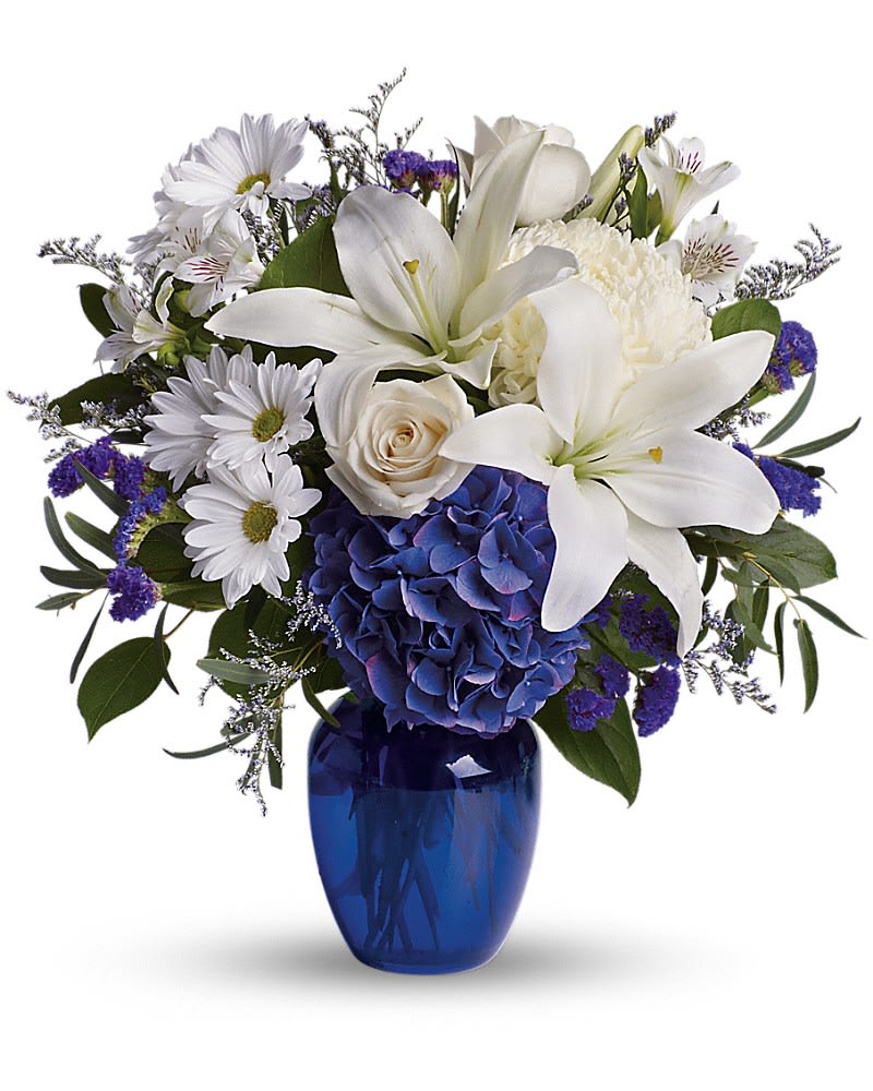Beautiful in Blue Beautiful in Blue - In this arrangement, the serenity of the color blue along with the purity of intention symbolized by white will let the family know you are sending your calm strength to them during these difficult times. Beautiful blooms such as blue hydrangea, crème roses, white lilies and alstroemeria along with white chrysanthemums, eucalyptus, limonium and more are beautifully arranged in a dazzling cobalt blue vase.Approximately 16 1/2" W x 18" H