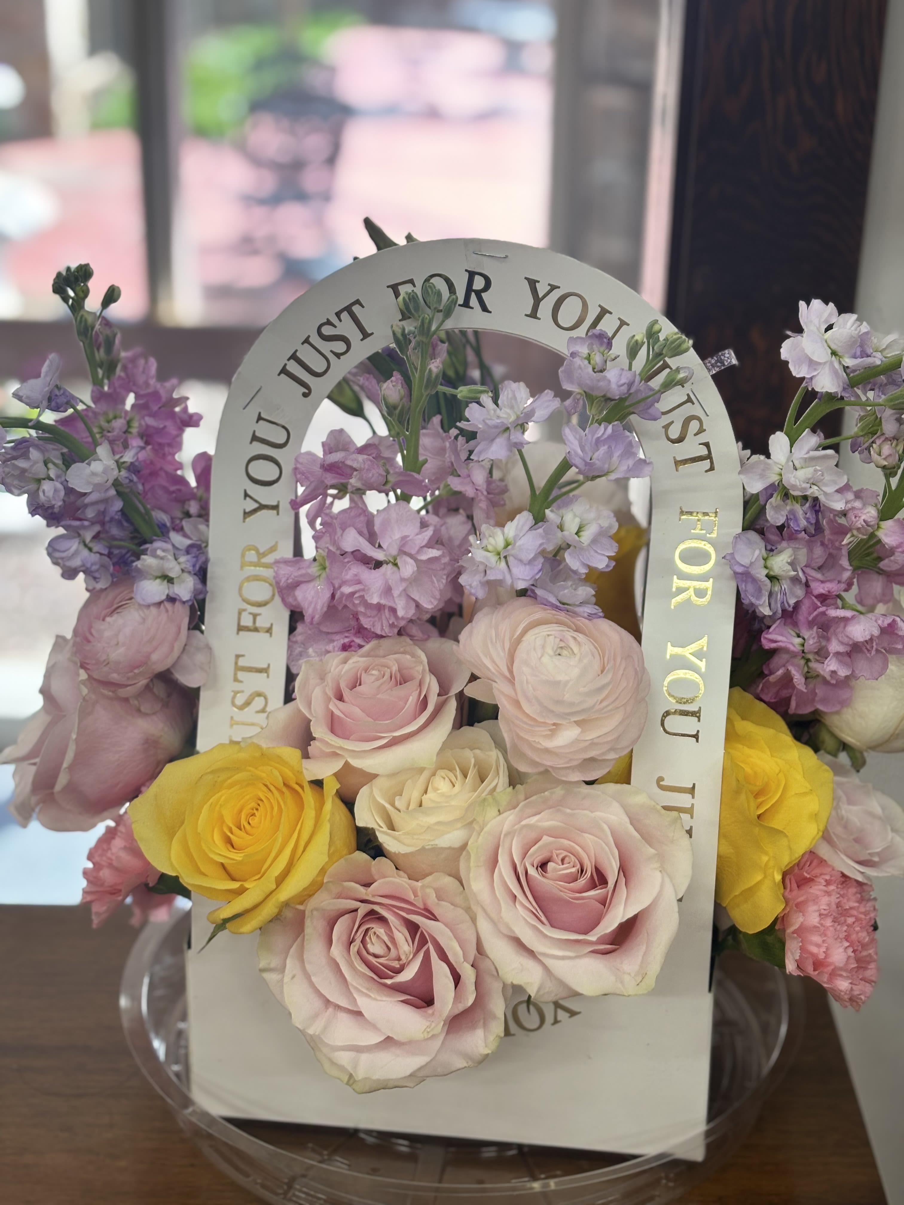 Chérie Fleur - Delicate, joyful, and effortlessly chic, Chérie Fleur is a celebration of affection in bloom. Featuring a dreamy blend of blush and ivory roses, cheerful yellow accents, and airy lavender stock, this handbag-style arrangement delivers all the elegance of a Parisian bouquet with a touch of playful romance. Whether given as a gift or displayed as a sweet indulgence, Chérie Fleur speaks softly but beautifully—just for you.