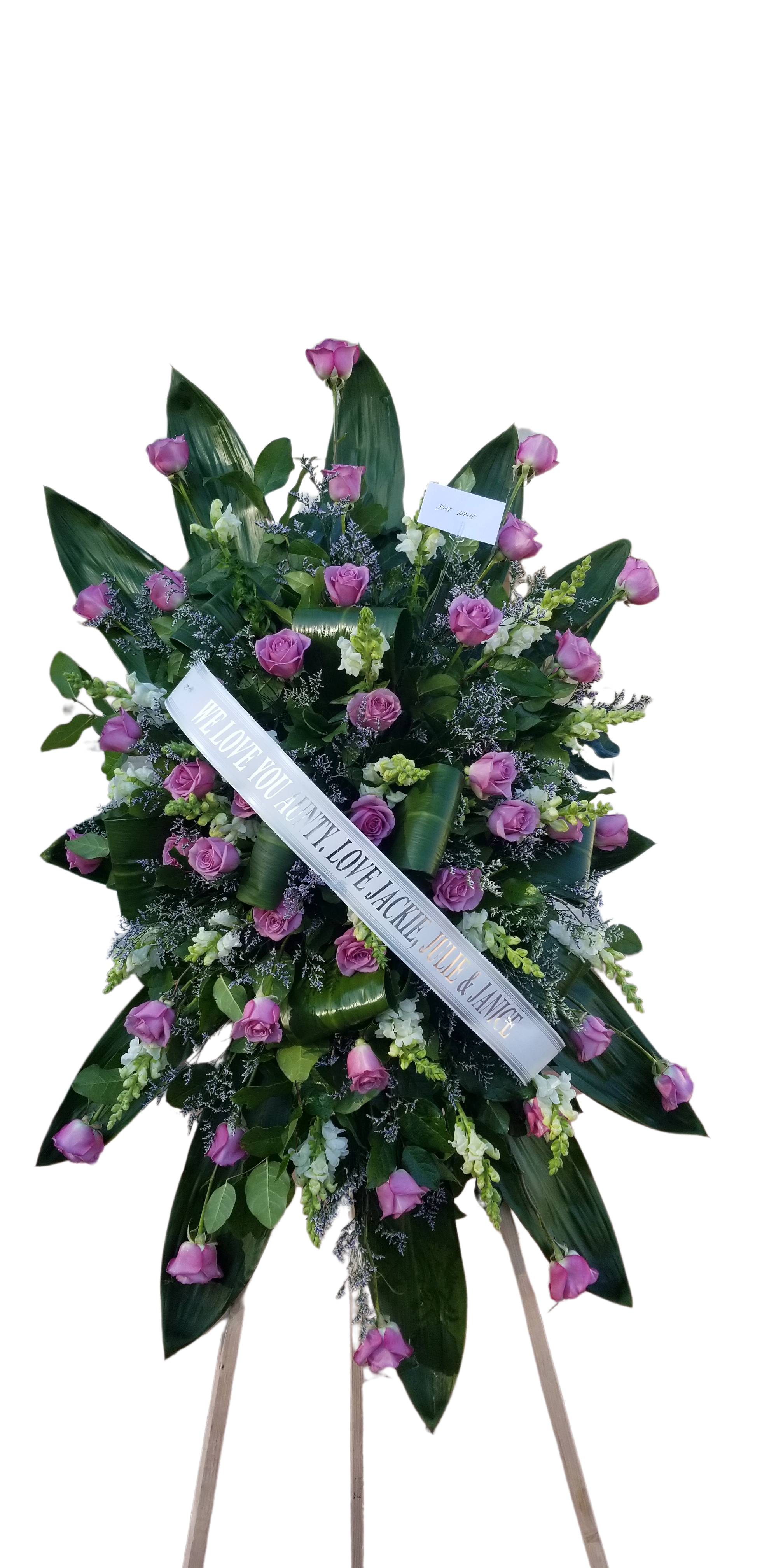 Lavender Rose Stand Up Spray - A lavender rose funeral spray is a beautifully composed floral arrangement that embodies elegance and serenity. The soft, muted hues of lavender roses symbolize grace, remembrance, and love, making them a poignant choice for honoring a loved one.   The arrangement often features a variety of lavender roses at different stages of bloom, which adds depth and texture. These are typically interspersed with lush greenery, such as eucalyptus or ferns, creating a soothing contrast. Accents like white lilies or delicate baby’s breath can enhance the overall composition, symbolizing purity and innocence.  The spray is usually designed to be displayed in a standing position, ideal for a casket or altar. Ribbons in complementary shades might be added for an extra touch of elegance, further conveying sentiments of love and peace. Overall, a lavender rose funeral spray serves as a heartfelt tribute, capturing the essence of the person being honored while providing comfort to those in mourning.