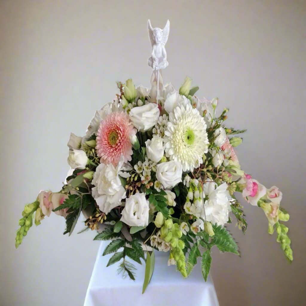 Cherub Blush - Cherub Blush presents an exquisite floral composition, artfully combining a vibrant selection of fresh flowers, including snapdragons, lisianthus, gerberas, poms, carnations, and wax flowers in gentle whites and light pinks, all beautifully complemented by a charming white angel pick.  When you request a custom design, we will strive to create something that closely mirrors the image you have in mind. Remember, each arrangement is one-of-a-kind and crafted specifically for you. Given the natural variability of flowers, some color substitutions may be necessary, and prices and availability of seasonal blooms can vary.
