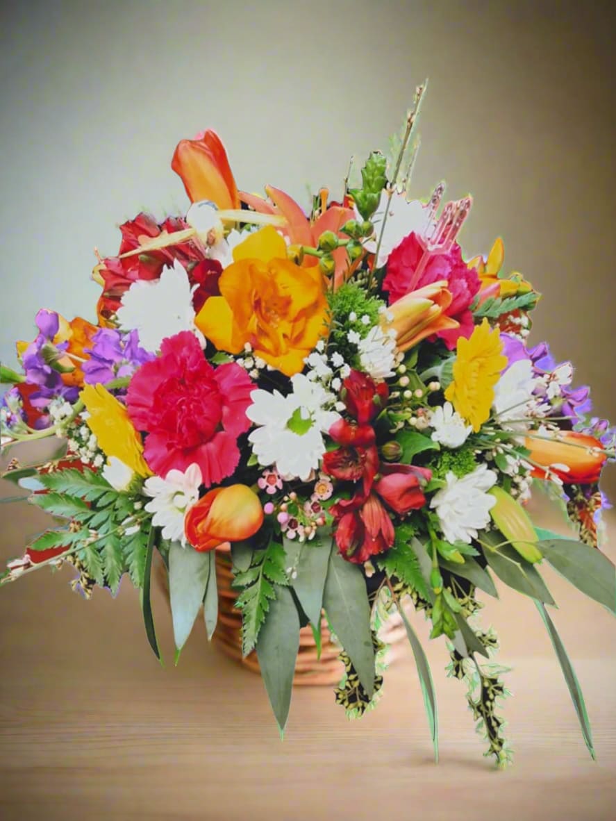 Cheerful Garden Delight - Cheerful Garden Delight is a vibrant and uplifting basket arrangement that showcases a delightful mix of tulips, stock, daisies, carnations, and alstromeria, all beautifully complemented by lush greenery. This arrangement offers a stunning contrast of bright colors against a backdrop of white, making it perfect for any occasion.  In creating our floral designs, we strive to closely mirror the envisioned concept. It's important to note that each arrangement is unique and customized just for you. Due to the natural variations in flowers, some adjustments in color may be required. Furthermore, please be aware that the prices and availability of seasonal flowers can fluctuate.