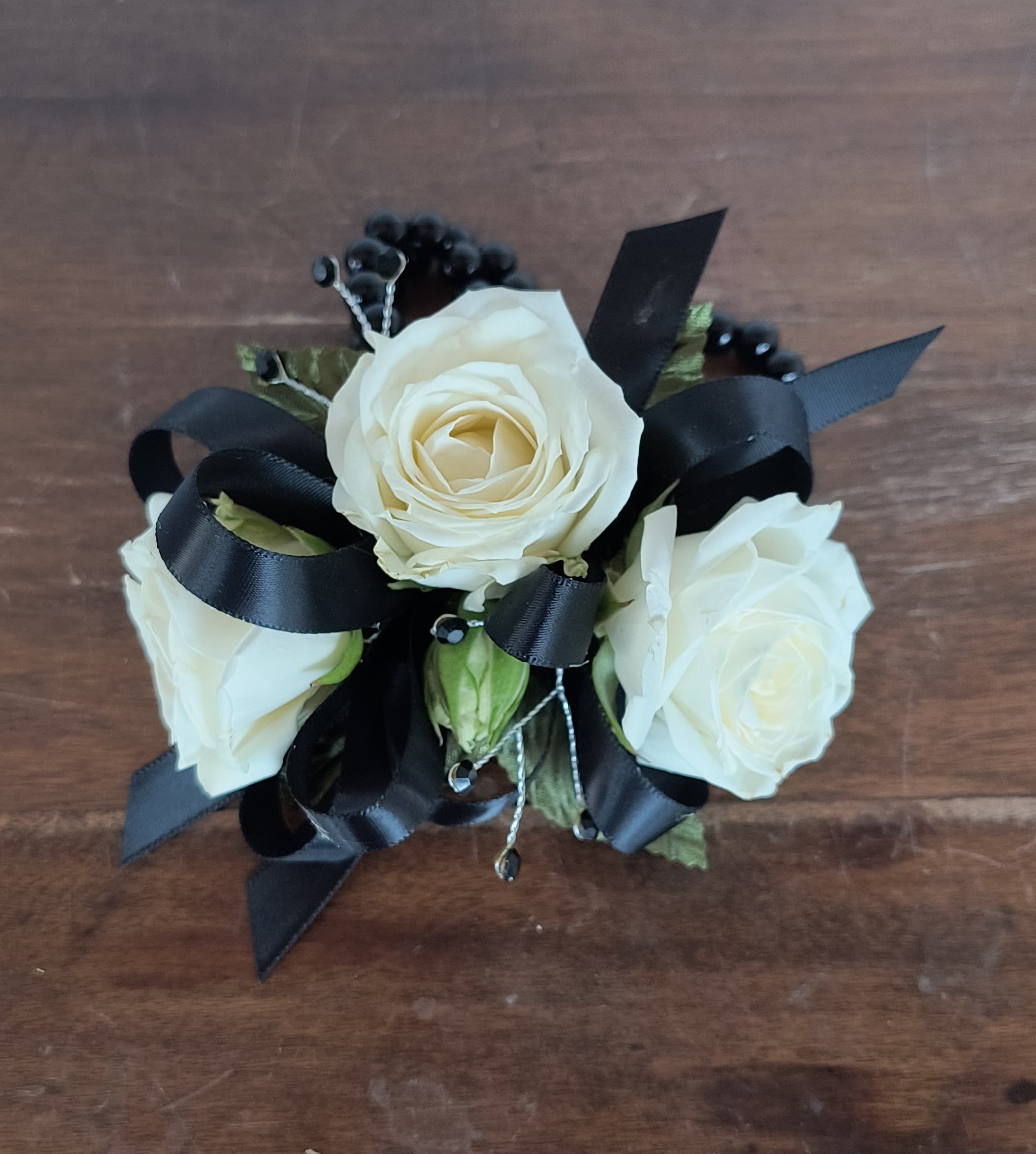 Onyx Wrist Corsage - Delicate white rose blooms are accented everything onyx. Black Ribbon, black gems and black pearl wristlet. Can be upgrade with fresh greens or filler flower even add an onyx rhinestone wristlet!