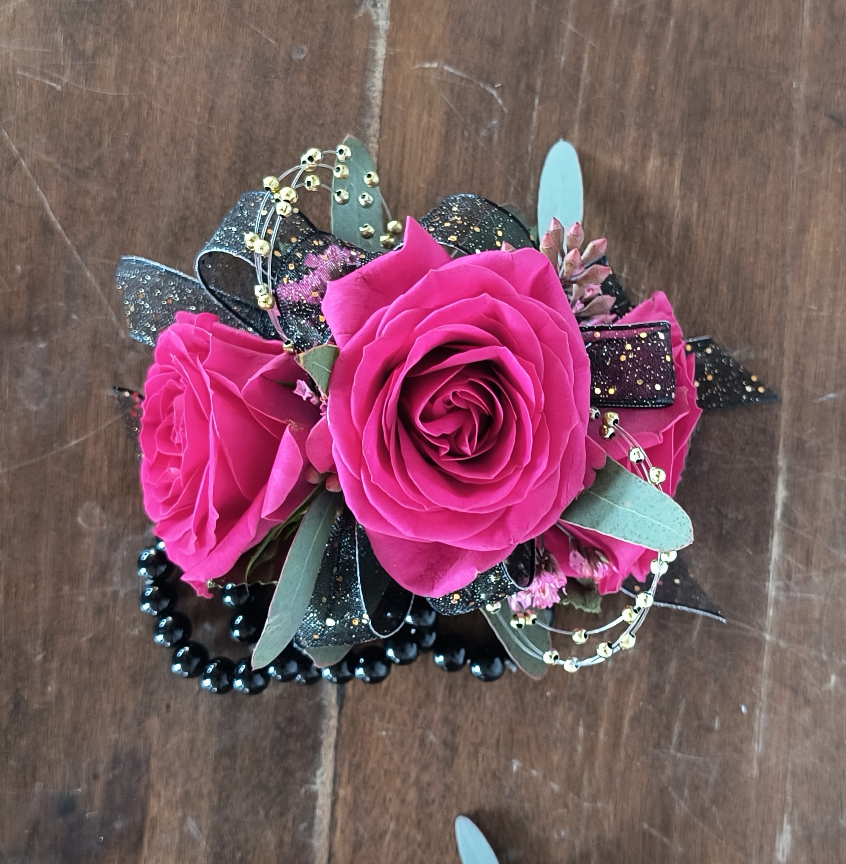 Pazazz Wrist Corsage Pazazz Wrist Corsage - Hot Hot Hot! Fuchsia spray rose and pink limonium filler with classic black and gold accents. Corsage includes a black pearl wristlet.