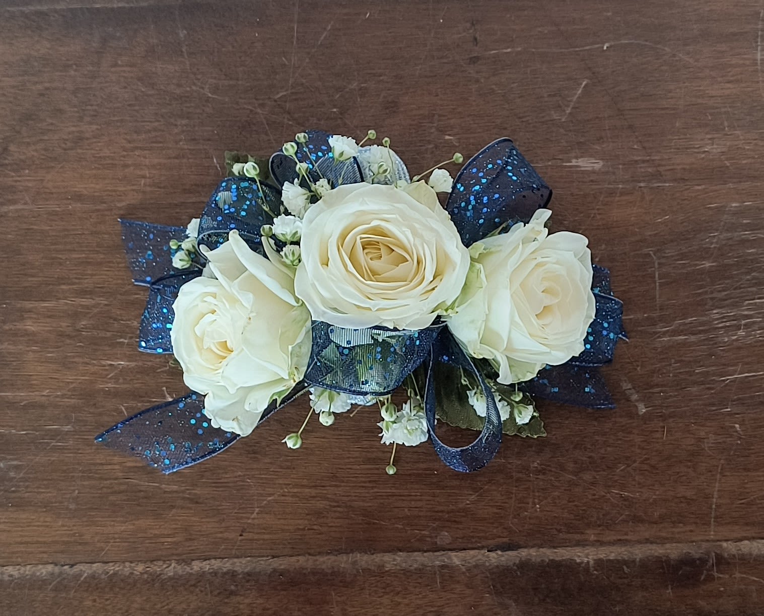 Royal Wrist Corsage Royal Wrist Corsage - Pure white spray rose and royal blue ribbon make this wrist corsage fit for royalty. Add some fresh greens to finish the look. Includes an elastic disposable wristlet.