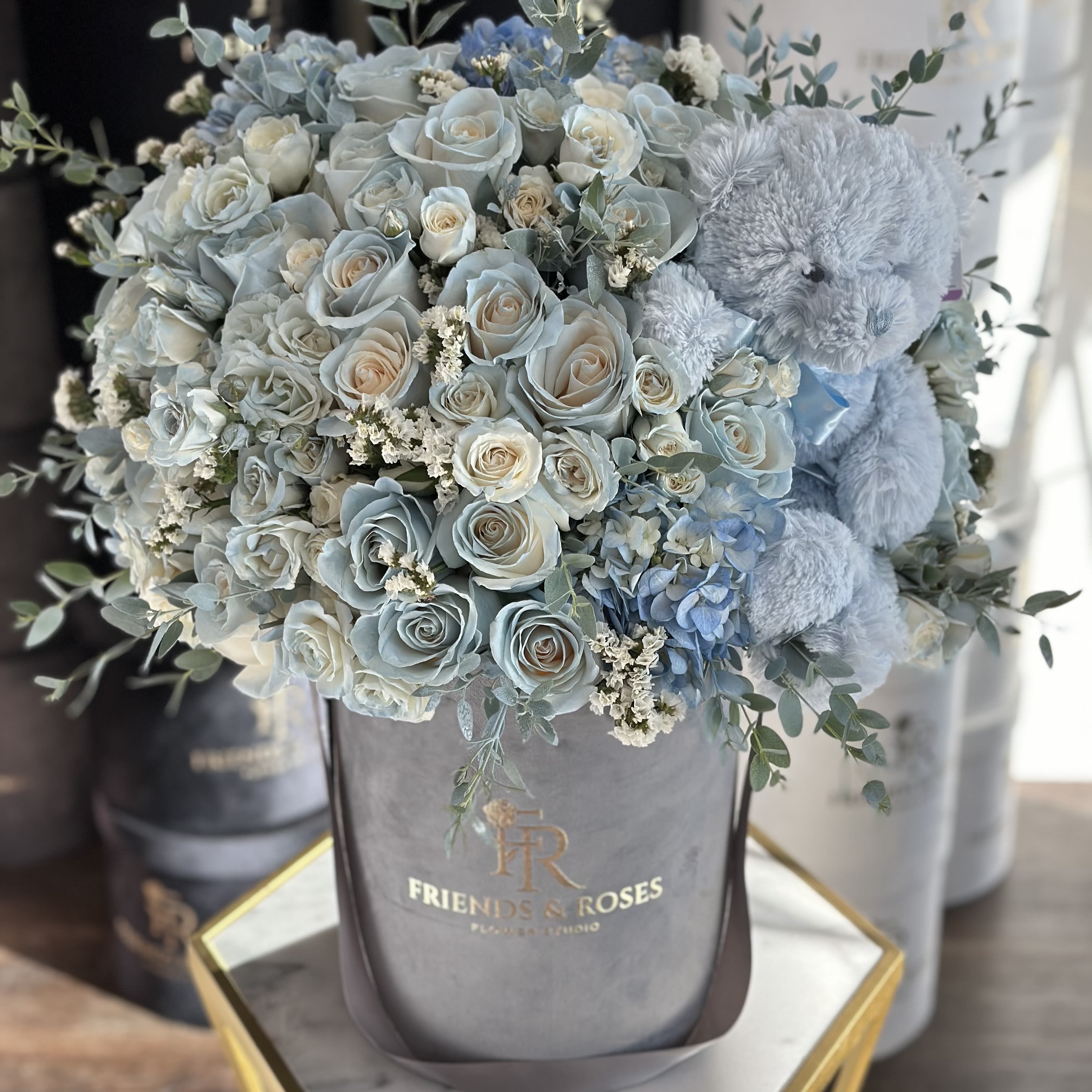Baby Teddy  - A charming bouquet in a  elegant box featuring soft blue roses and hydrangeas , paired with an adorable teddy bear , perfect for celebrating the arrival of a newborn boy . This thoughtful arrangement combines sweetness and serenity for a heartfelt welcome.  May be in a pink color by request