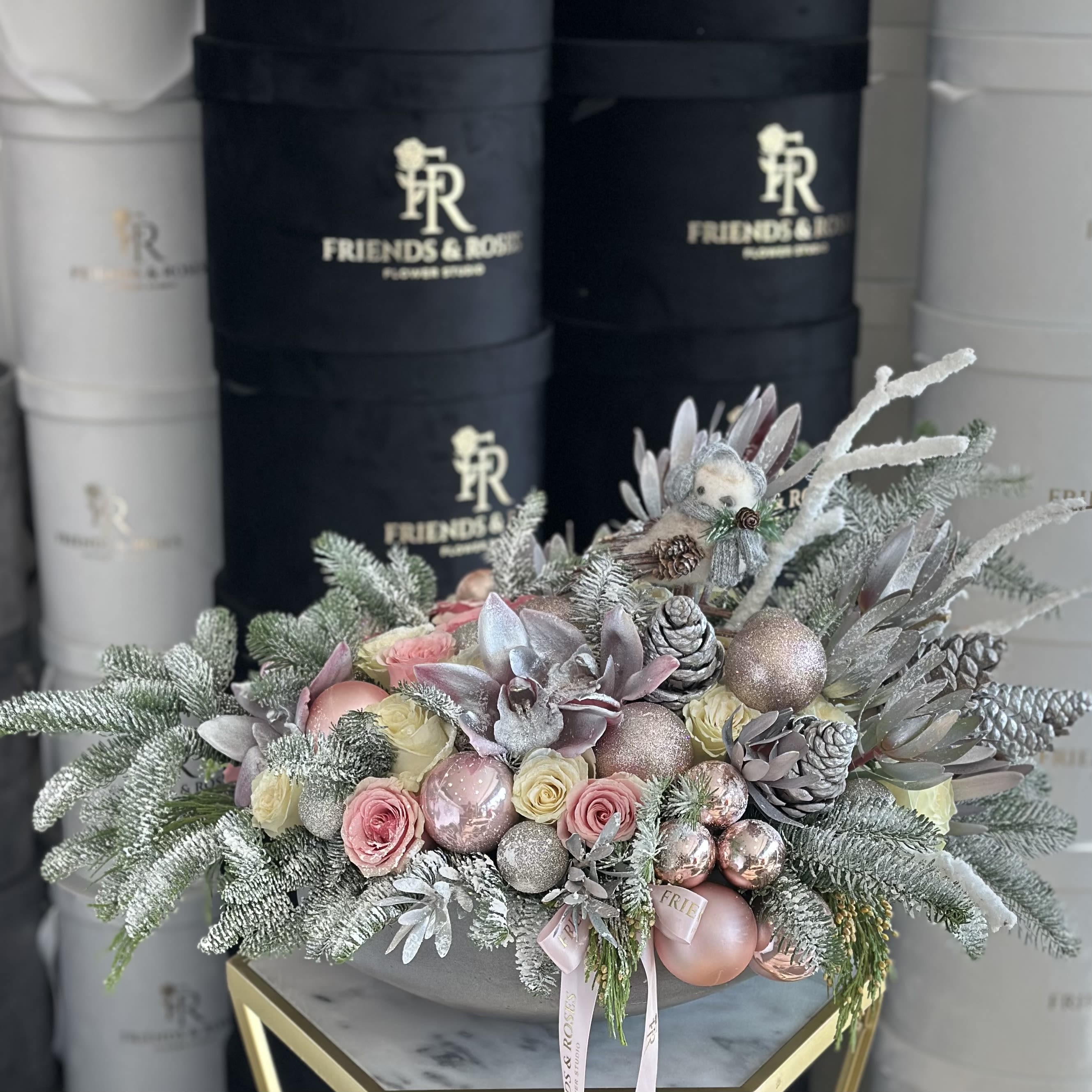 Christmas Carol - The &quot;Christmas Carol&quot; arrangement in an art vase combines delicate pink and white roses, lush fir branches, festive pink Christmas tree toys, pine cones dusted with snow, and a charming little bird, evoking the warmth and joy of the holiday season.