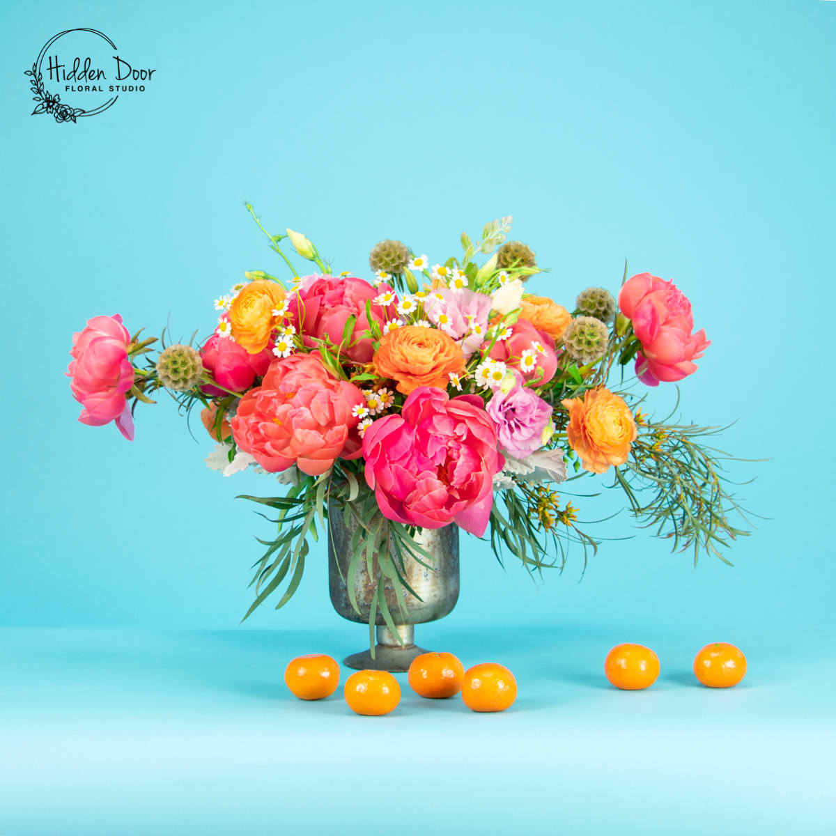 Virtuoso Virtuoso - Virtuoso Arrangement Discover the "Virtuoso," a floral symphony blending elegance and play. This modern masterpiece shines with vibrant pink peonies and lively orange ranunculus, arranged asymmetrically for artistic flair. Each bloom is carefully placed, weaving grace with bold energy. Set in an antique glass vase, its vintage charm enhances the design, while seasonal greens add depth and harmony. Perfect for daily joy, weddings, or corporate events, "Virtuoso" enhances any space with sophistication. Its playful beauty brings delight, making every moment special. Crafted by Hidden Door Floral Studio, this arrangement reflects our passion for excellence. Ideal for Triangle celebrations, it’s a gift that impresses.