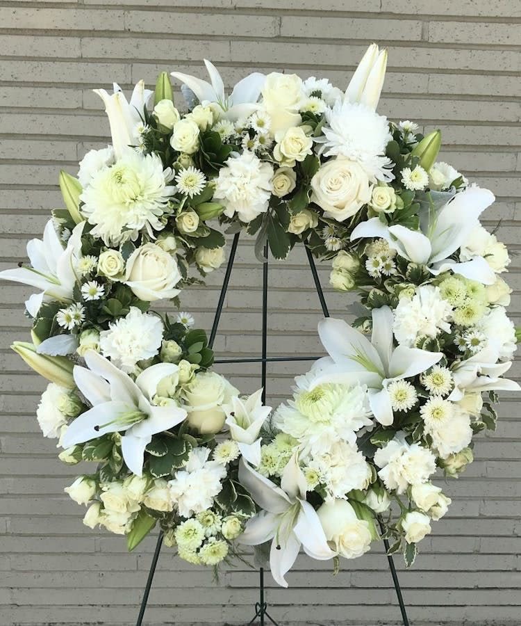 White Funeral Wreath - White funeral wreath offers peaceful wishes of heartfelt sympathy with each delicate bloom. White roses, white oriental lillies, spray roses, cushion and more foliage. Displayed on a wire easel