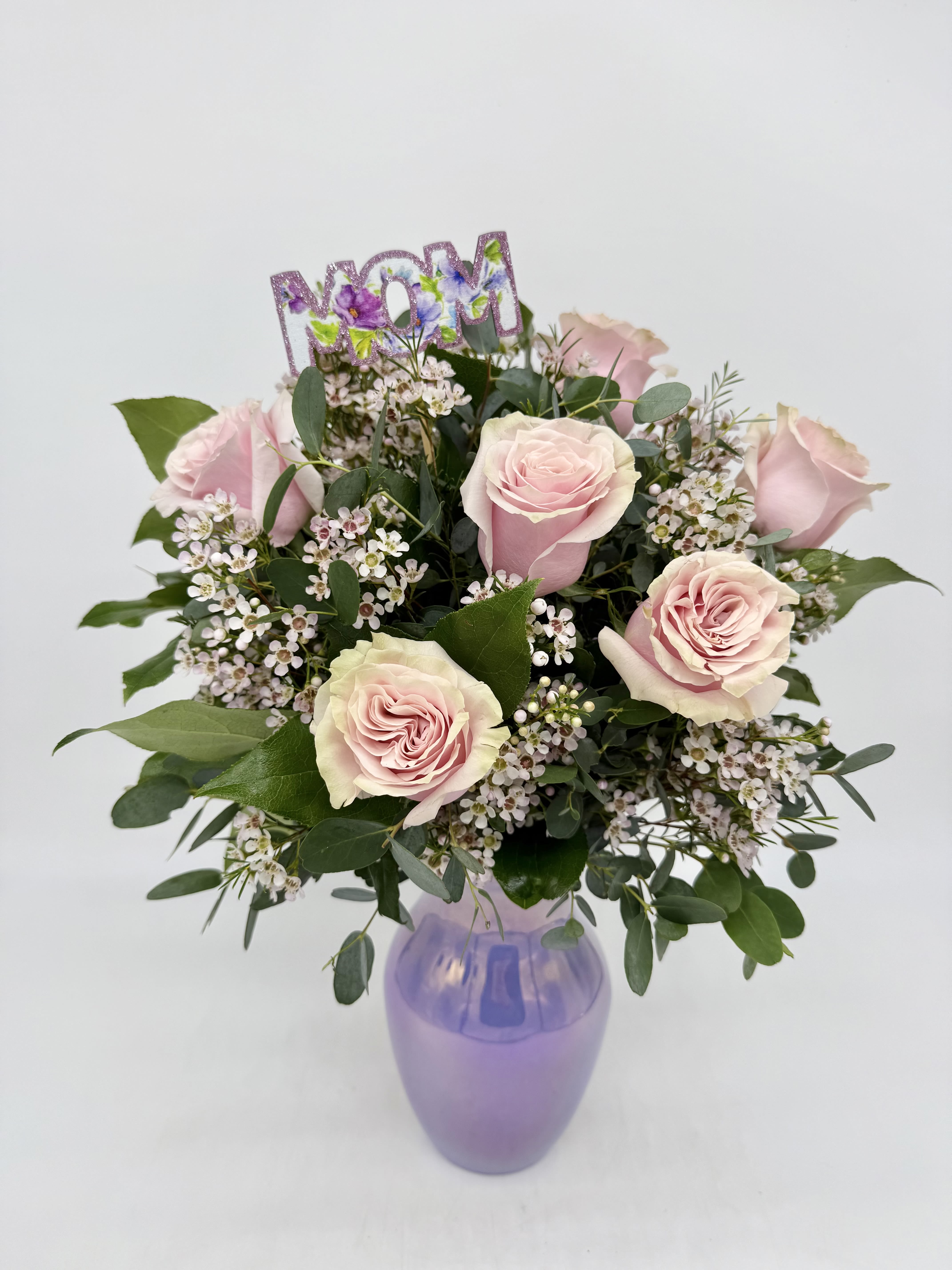 LF412 Half Dozen for Mom LF412 Half Dozen for Mom - Celebrate Mom with this elegant arrangement featuring soft blush roses, white wax flowers, and lush greenery, all beautifully displayed in a radiant lavender vase. The shimmering "MOM" topper adds a heartfelt touch. It's the perfect gift to brighten her day and express your love this Mother's Day