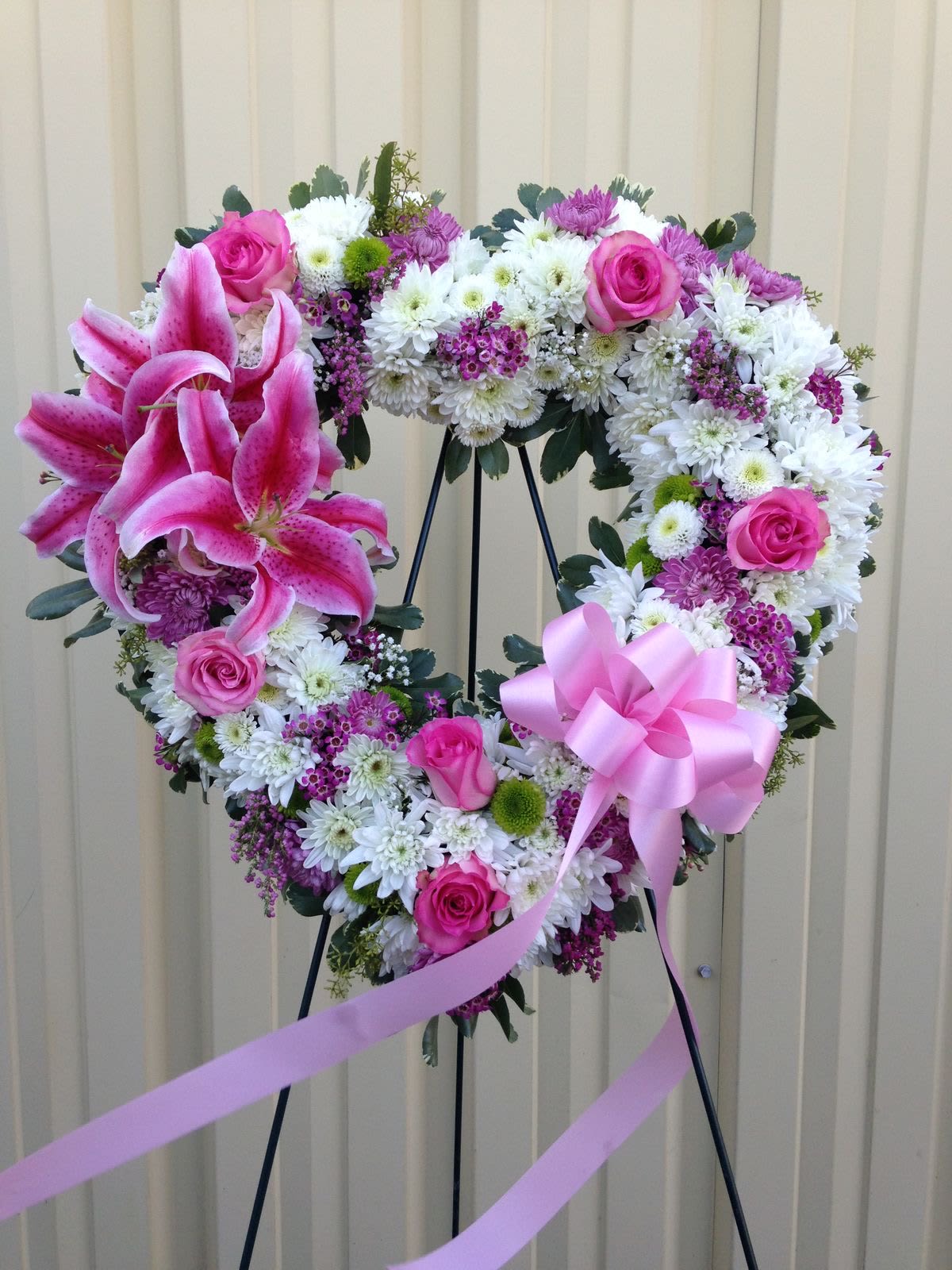 Angel Heart - Our beautiful heart of funeral flowers to create a touching tribute that will show your loved ones how much you care.  Open, heart-shaped arrangement of pink lilies, pink roses, daisies and pink wax flower designed on an easel and accented with satin ribbon, appropriate for the funeral home.
