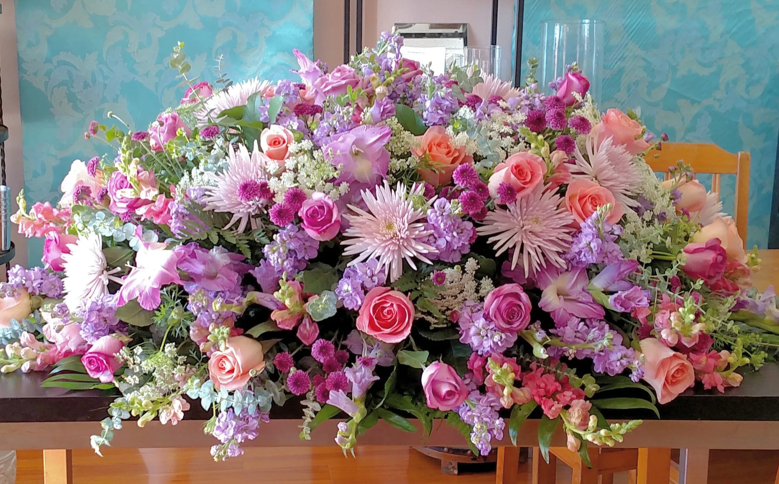 Large Pastel Casket Spray Large Pastel Casket Spray - This large casket spray has 3 dozen roses, gladiola, snap dragon, spider mums, queen anns lace, stock and several Pastel filler flowers that give this soft beautiful look to any casket color.