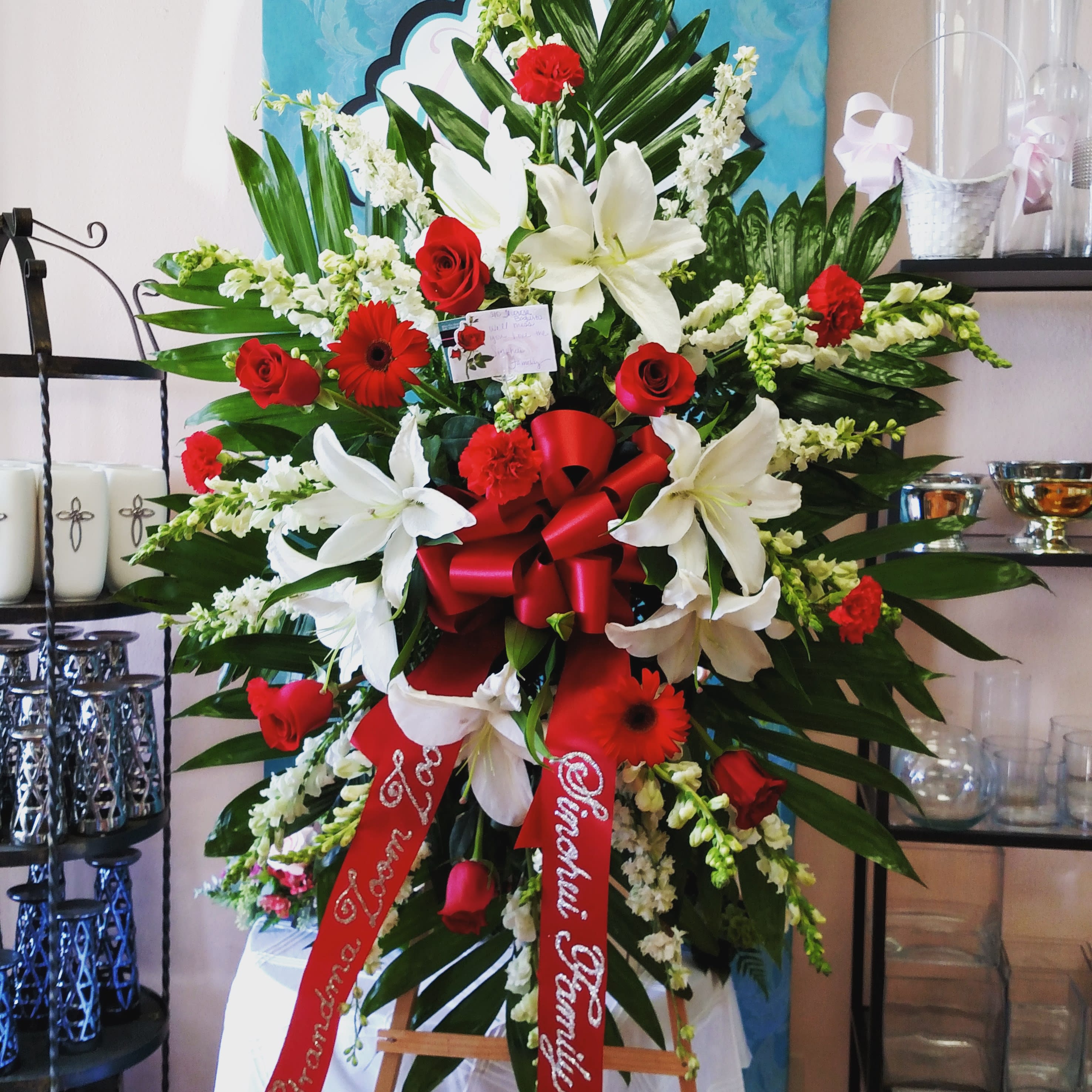 Love And Prayers Sympathy Spray - This spray has red roses, large big white lilies, red Gerber daisies, and carnations. Bow included, the wording is not. For a custom banner, please add by searching &quot;Sympathy Banner&quot;.