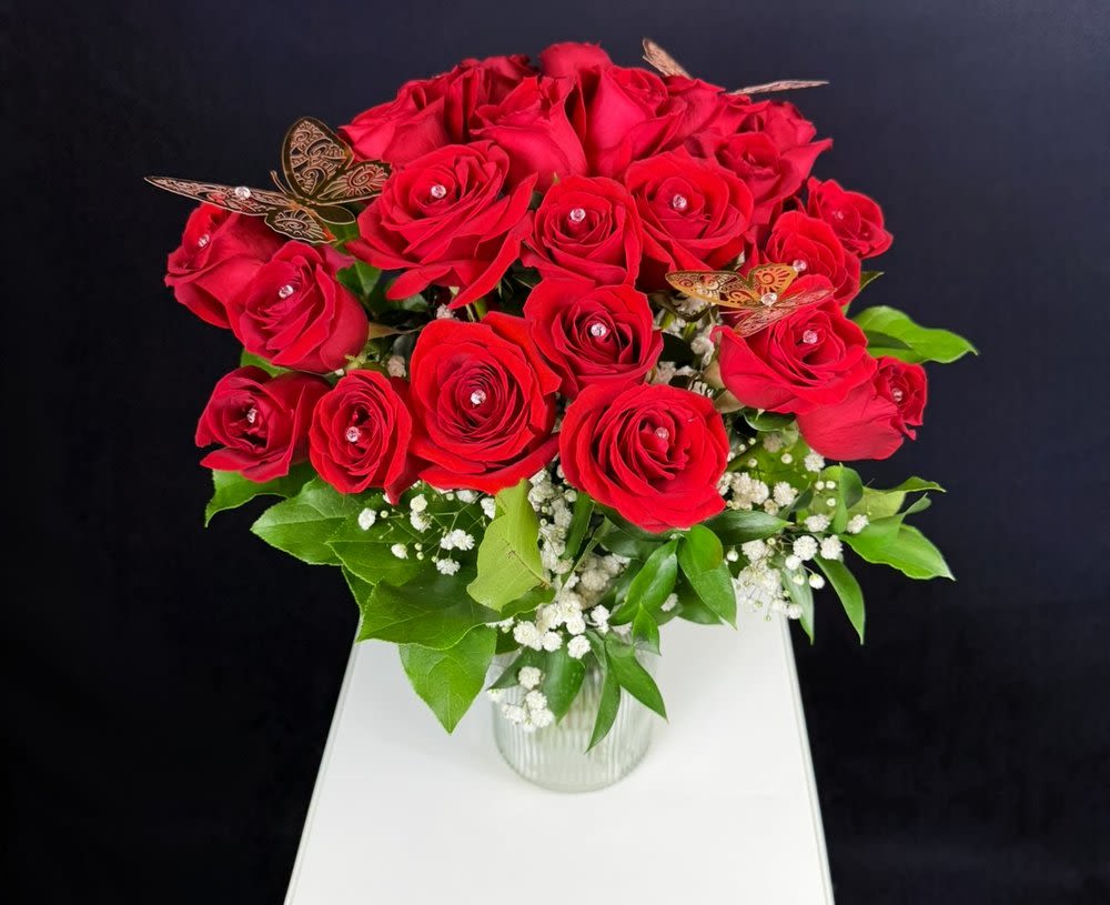 24-Red Roses Vase Arrangement 24-Red Roses Vase Arrangement - The Queen Vase Arrangement The Queen Vase Arrangement is a striking, medium-sized bouquet that brings a bold and elegant statement. Featuring 24 rich, vibrant roses, this arrangement is designed to impress and make a lasting impression. Accented with soft baby’s breath for a delicate touch, and adorned with shimmering gold metallic butterflies and sparkling diamond-shaped stones, each rose is elevated with subtle elegance. The Queen Arrangement is displayed in a beautiful glass vase, one that the recipient can keep and reuse, making this gift even more thoughtful and lasting. The vase adds a refined, timeless touch, and with the larger size of the arrangement, it’s sure to make a grand impression. This larger arrangement means more flowers, more beauty, and more impact, making it the perfect way to show someone just how special they are. The Queen Vase Arrangement combines romance and sophistication in one stunning package. It also comes with a small message card from the sender, allowing you to personalize your gesture with a heartfelt note.