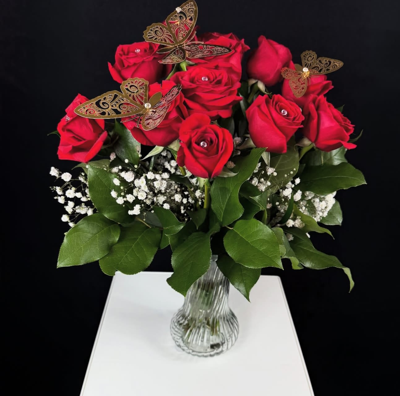  12 Red Roses in Vase - The Princess Vase Arrangement  The Princess Vase Arrangement is a charming, smaller version of our larger Queen Mother Vase Arrangement, more elaborate designs, offering the same exquisite beauty in a more delicate and affordable size. This stunning bouquet features 12 rich red roses, accented with soft baby’s breath for a light, airy touch. Delicate gold metallic butterflies and sparkling diamond-shaped stones embellish each rose, adding a subtle shimmer and extra elegance.  What makes this arrangement even more special is that it comes arranged in a beautiful glass vase, one that the recipient can keep and reuse. The vase adds a refined and timeless elegance to the flowers, making the gift even more thoughtful and lasting.  It also comes with a small message card from the sender, allowing you to personalize your gesture with a heartfelt note.