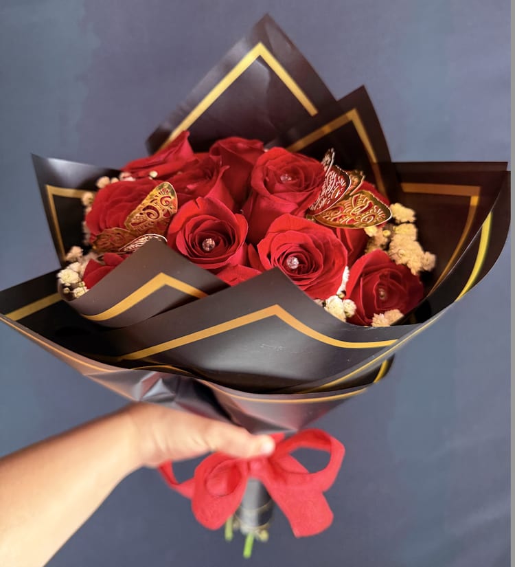  12-Red Roses Bouchon Bouquet - Small Bouchon Bouquet  For those who appreciate a subtle yet meaningful gesture, the Small Bouchon Bouquet offers a refined and delicate expression of love. This beautiful arrangement, featuring 12 carefully selected red roses, is perfect for conveying admiration in a more understated, yet still heartfelt way. With its classic design, this bouquet radiates elegance and romance, enhanced by soft baby’s breath and delicate sparkling diamond-shaped stones on each rose. It’s further accentuated by charming gold metallic butterflies, adding a touch of whimsy and sophistication.  Finished with a sleek black ribbon, the Small Bouchon Bouquet is an ideal choice for those who enjoy the beauty of simplicity with a refined touch. Whether it's a romantic gesture or a thoughtful gift for someone special, this bouquet will surely brighten their day and leave a lasting impression.  A small message card accompanies this arrangement, allowing you to add a personal note that speaks directly from the heart.