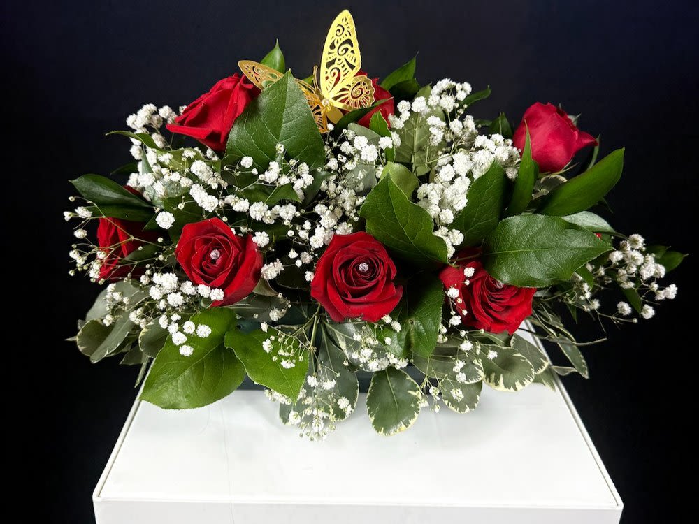 12-Roses Garden Arrangement - The Royal Garden  This stunning garden rose arrangement brings the elegance of a royal garden right into your space. Set on an oasis base, it showcases a lush variety of greenery, creating a rich, textured backdrop for 12 exquisite roses. Each rose is uniquely enhanced with a sparkling stone nestled inside, adding a touch of magic and sophistication. The arrangement is further adorned with beautiful metallic butterflies, delicately perched atop the flowers, giving it a whimsical, yet regal touch. Perfect for tables or as a centerpiece, this medium-sized arrangement effortlessly combines nature's beauty with artistic design, making it an ideal choice for any occasion.  It also comes with a small message card from the sender, allowing you to personalize your gesture with a heartfelt note.