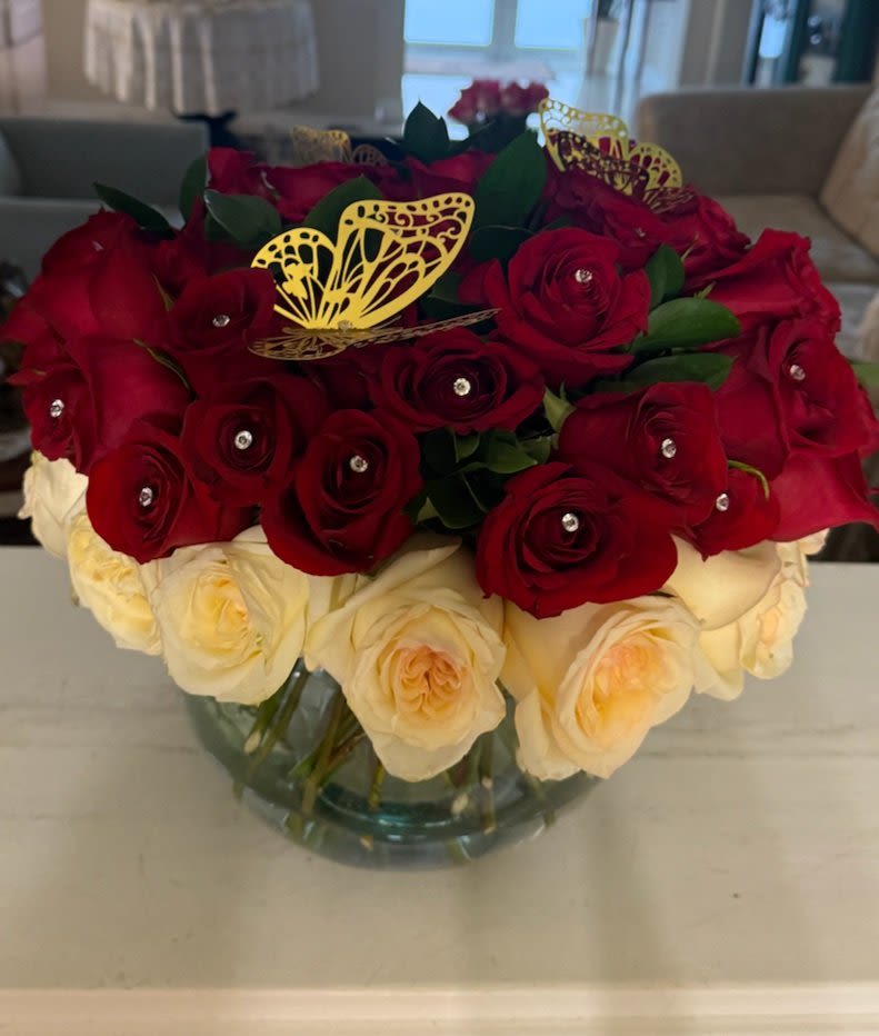 &quot;Queen of Hearts” Jewel Rose Bowl - &quot;Queen of Hearts” Jewel Rose Bowl  Make a grand gesture with our **“Queen of Hearts” Jewel Rose Bowl**, an opulent centerpiece bursting with passion and elegance. This luxurious round arrangement features rich red roses crowned with sparkling rhinestone pins, encircled by creamy ivory blooms for a stunning contrast. Delicate golden butterflies add a whimsical, regal finishing touch.  Arranged in a clear glass bowl, this floral masterpiece is perfect for romantic occasions, upscale events, or as a show-stopping gift for someone who deserves the world.  Details: - Hand-arranged premium red and ivory roses   - Red roses adorned with rhinestone accents   - Gold metallic butterflies for added charm   - Designed in a modern glass bubble vase   - Ideal for Valentine’s Day, anniversaries, or luxe décor   A bouquet fit for royalty—because love should always sparkle.