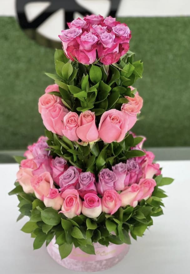 “Rosé Royale” 3-Tier Rose Tower “Rosé Royale” 3-Tier Rose Tower - “Rosé Royale” 3-Tier Rose Tower Turn every occasion into a celebration of beauty and grace with our **“Rosé Royale” 3-Tier Rose Tower**. This grand floral statement features layers upon layers of hand-selected roses in radiant shades of pink, lavender, and blush—each tier framed with lush green foliage for an exquisite, garden-fresh finish. Meticulously arranged to resemble a royal cake, this show-stopping piece is a favorite for birthdays, bridal showers, baby reveals, and luxe event décor. Feminine, fresh, and full of charm—it’s a floral sculpture designed to impress. **Details:** - Over 60 premium long-stem roses in ombré tones - Triple-tiered design with vibrant greenery accents - Arranged in a sturdy velvet-finish floral hat box base - Ideal for special occasions, romantic gifts, or centerpiece décor **Celebrate in style with this floral tower of love and elegance.**