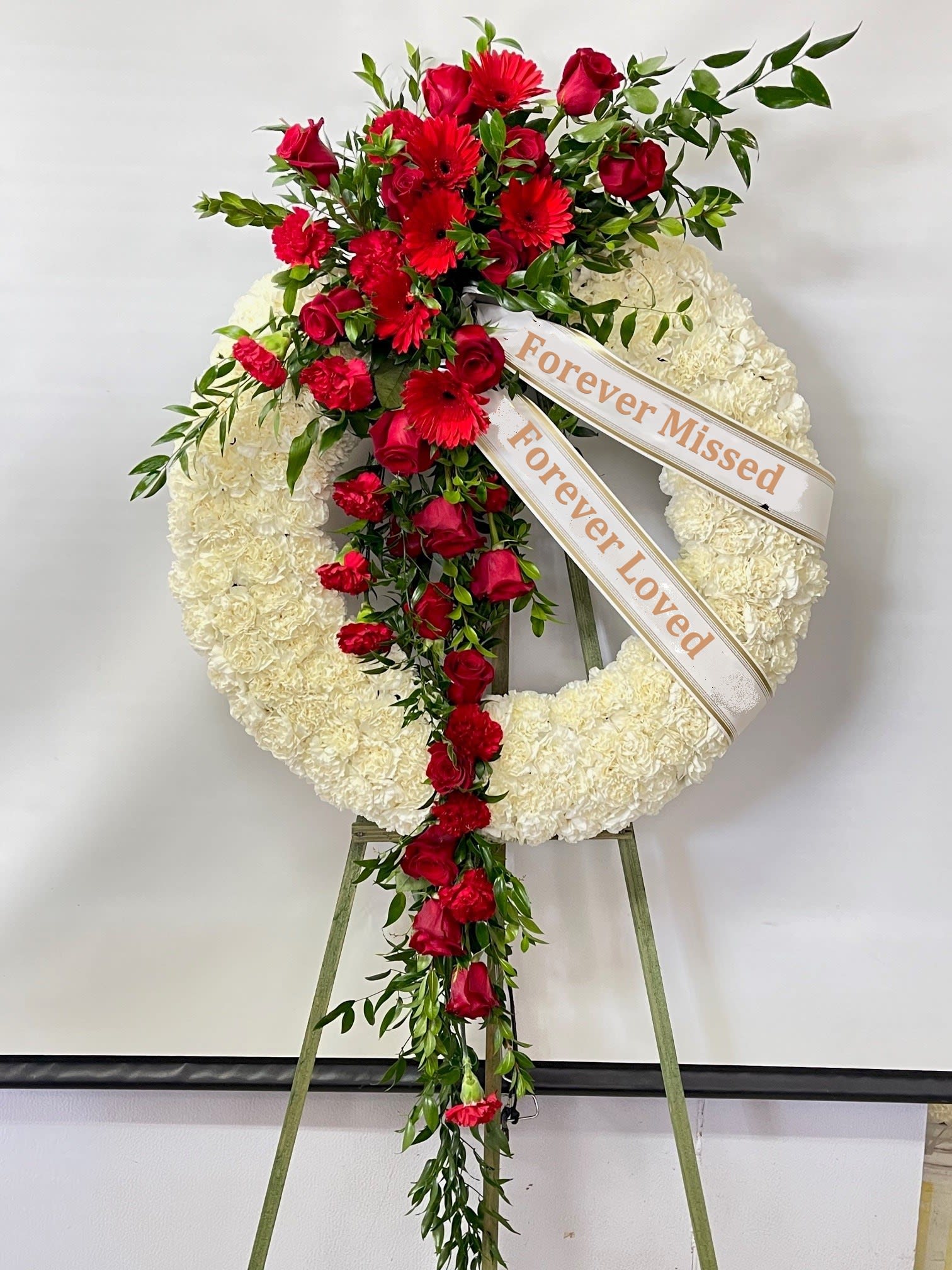 Sympathy Wreath #63 Sympathy Wreath #63 - Standing wreath made of all white flowers embellished with an all red cluster of fresh cut flowers. Colors can be modified depending on availability. Designed on an easel that is included with the arrangement and does NOT need to be returned. Banners are included with arrangement. Please specify what is to be printed on each banner upon check out under "FLORIST INSTRUCTIONS". LIMITED TO 5 WORDS PER BANNER.