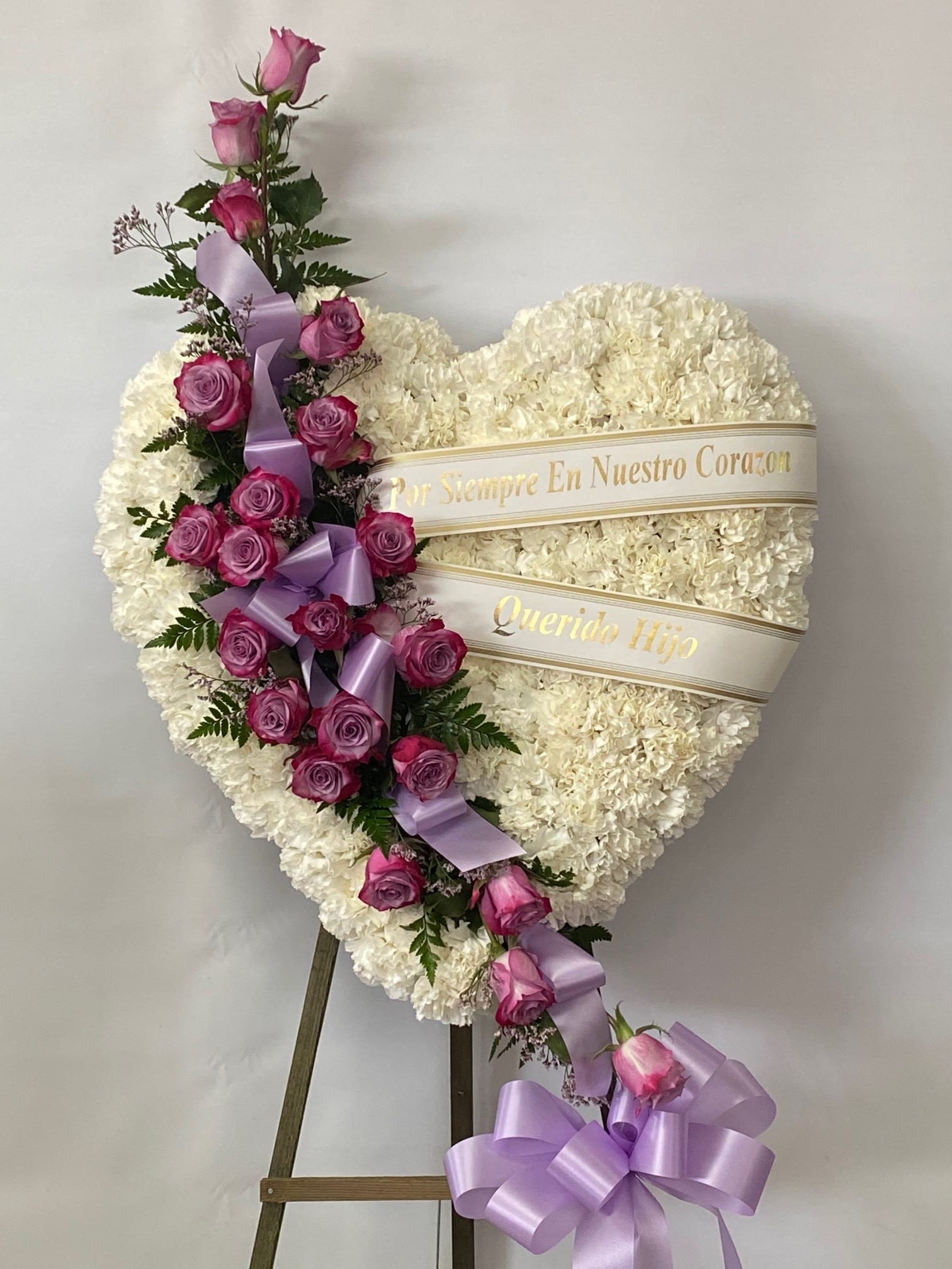 Sympathy Solid Heart #64 Sympathy Solid Heart #64 - All white standing heart embellished with a cluster of lavender roses and lavender ribbon. Colors can be modified depending on availability. Designed on an easel that is included with the arrangement and does NOT need to be returned.Banners are included with arrangement. Please specify what is to be printed on banner upon check out under "FLORIST INSTRUCTIONS". LIMITED TO 5 WORDS ON BANNER. If no note is added as to what to put NO banner will be added.