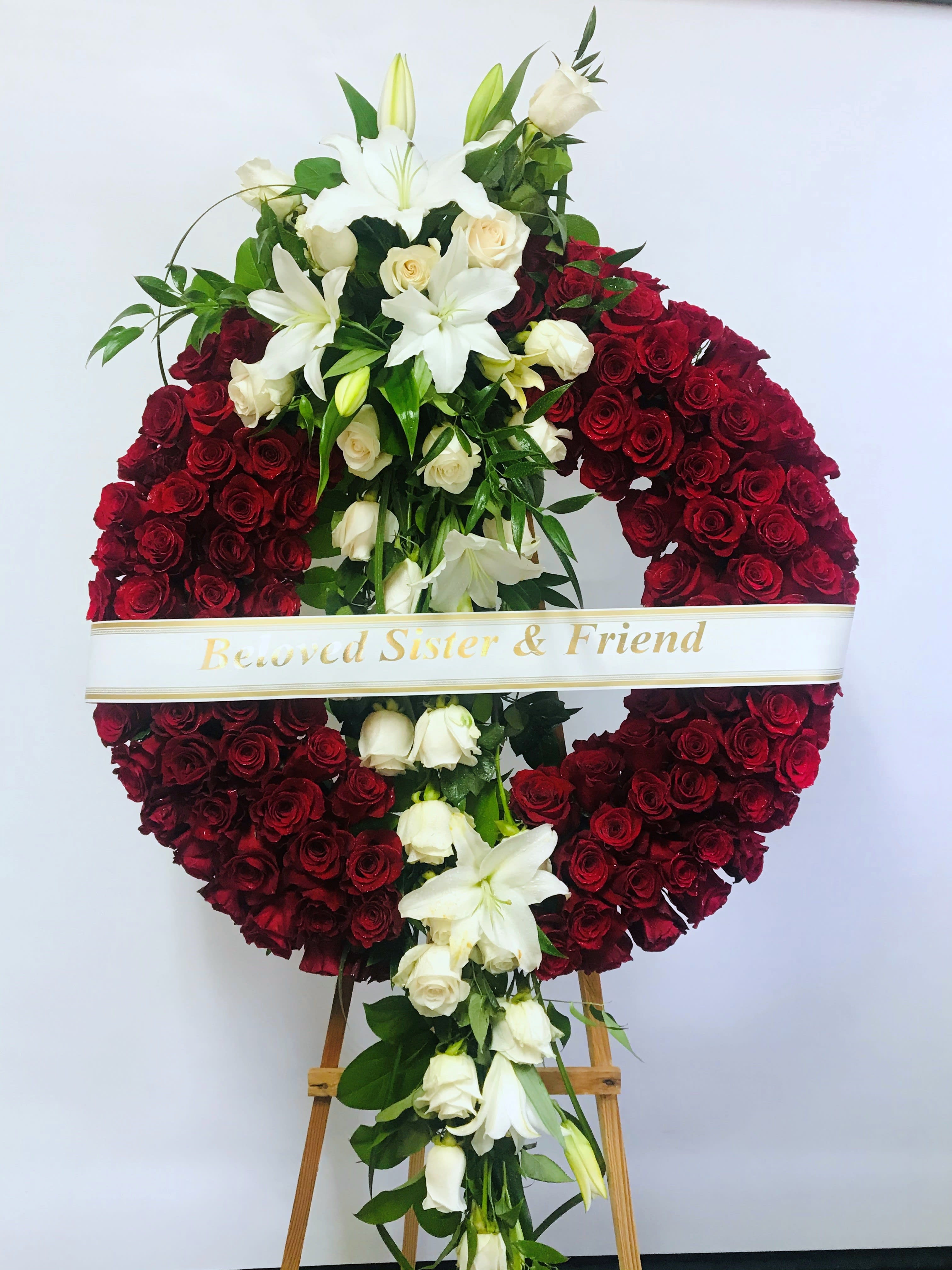 Sympathy Wreath #67 Sympathy Wreath #67 - All red standing wreath made of roses. Embellished with a cluster of white roses and lilies. Colors can be modified depending on availability. Designed on an easel that is included with the arrangement and does NOT need to be returned. Banner NOT included.