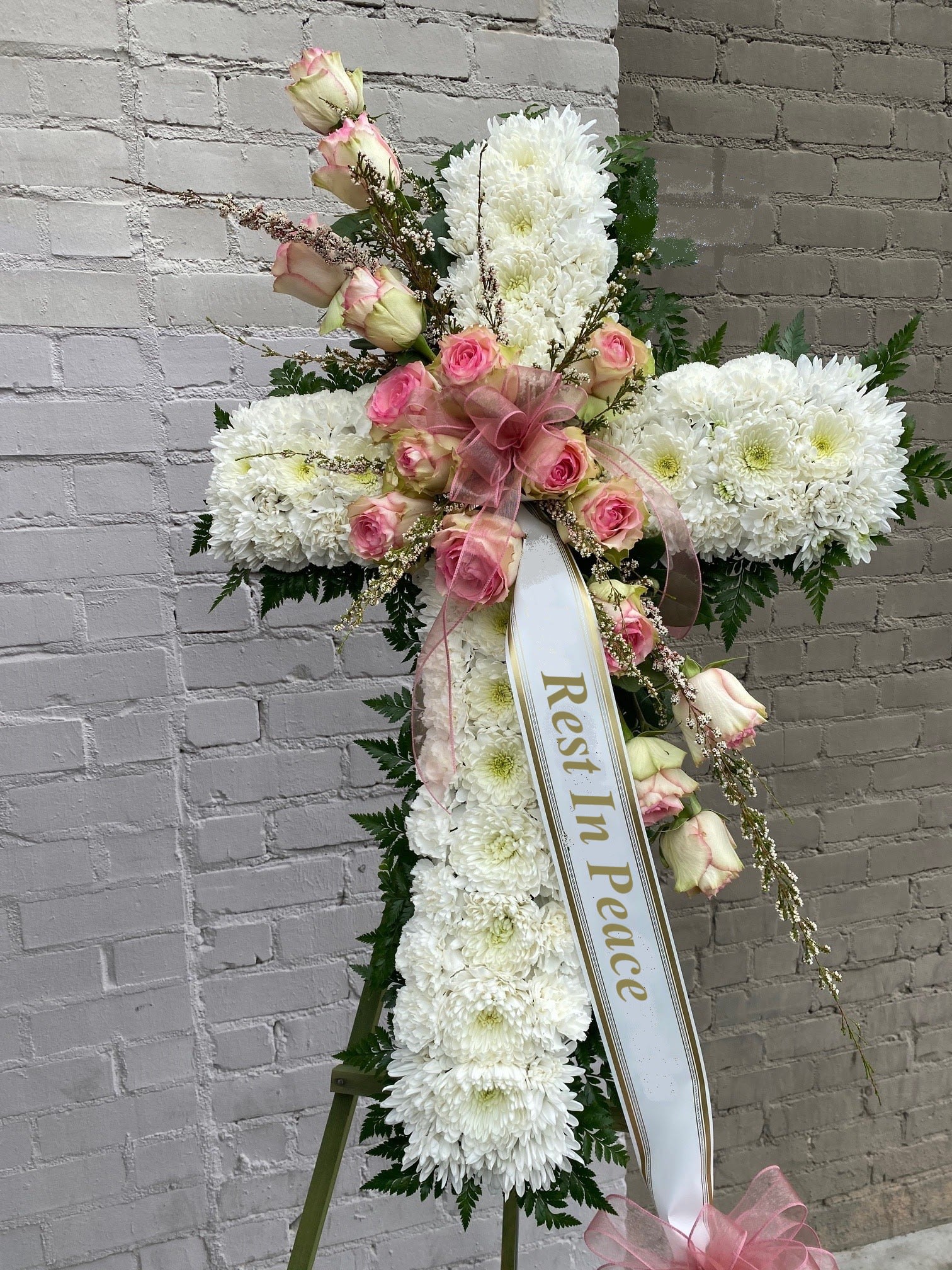 Sympathy Cross #41 - All white standing cross with a cluster of pink fresh cut flowers. Colors can be modified depending on availability. Designed on an easel that is included with the arrangement and does NOT need to be returned. Banner is included with arrangement. Please specify what is to be printed on banner upon check out under &quot;FLORIST INSTRUCTIONS&quot;. LIMITED TO 5 WORDS ON BANNER.