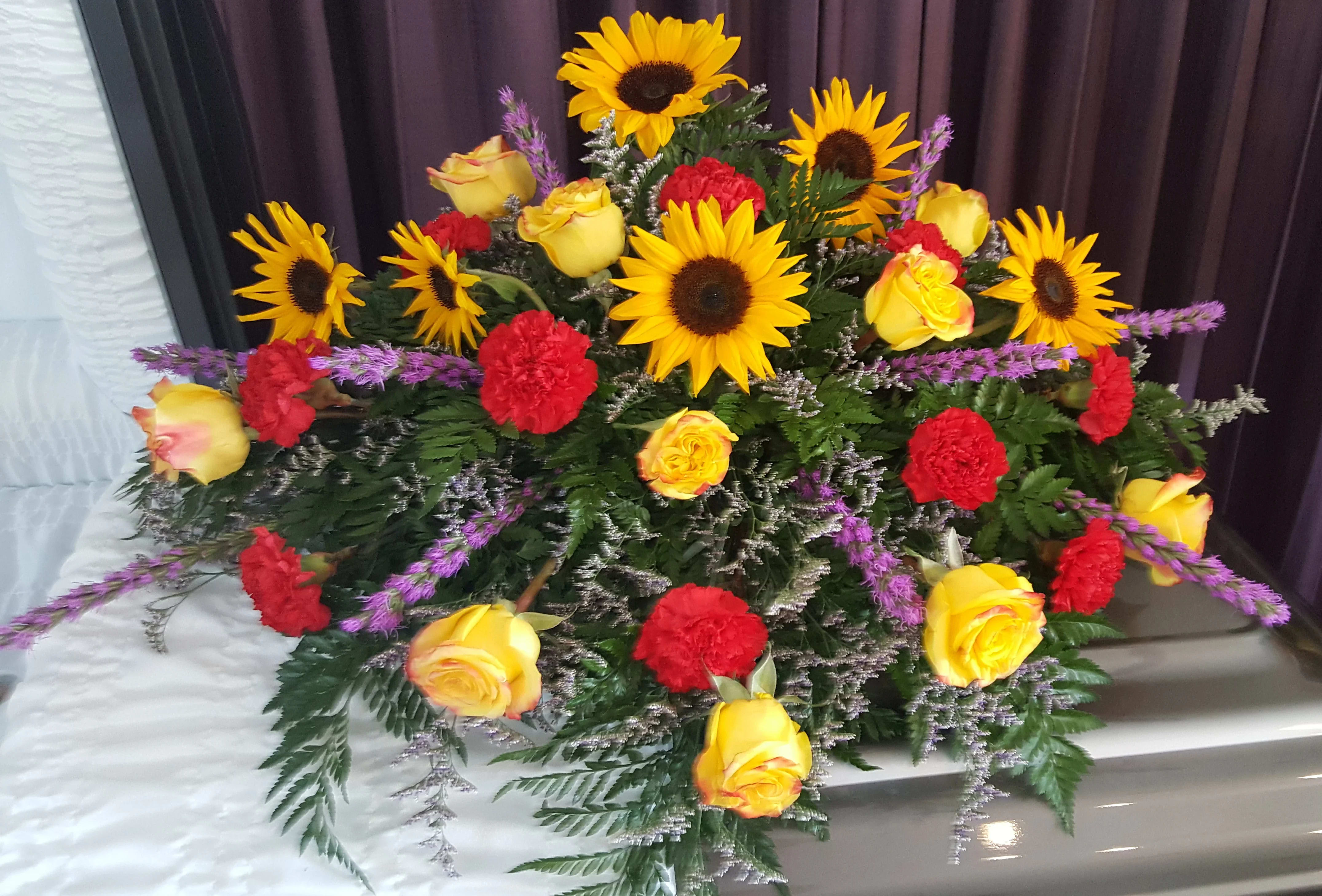 Sunflower and Roses Casket Spray Sunflower and Roses Casket Spray - Yellow Roses, Sunflowers, red carnations, Purple Liatris Please order at least 48 hours before service for all casket piece arrangements.