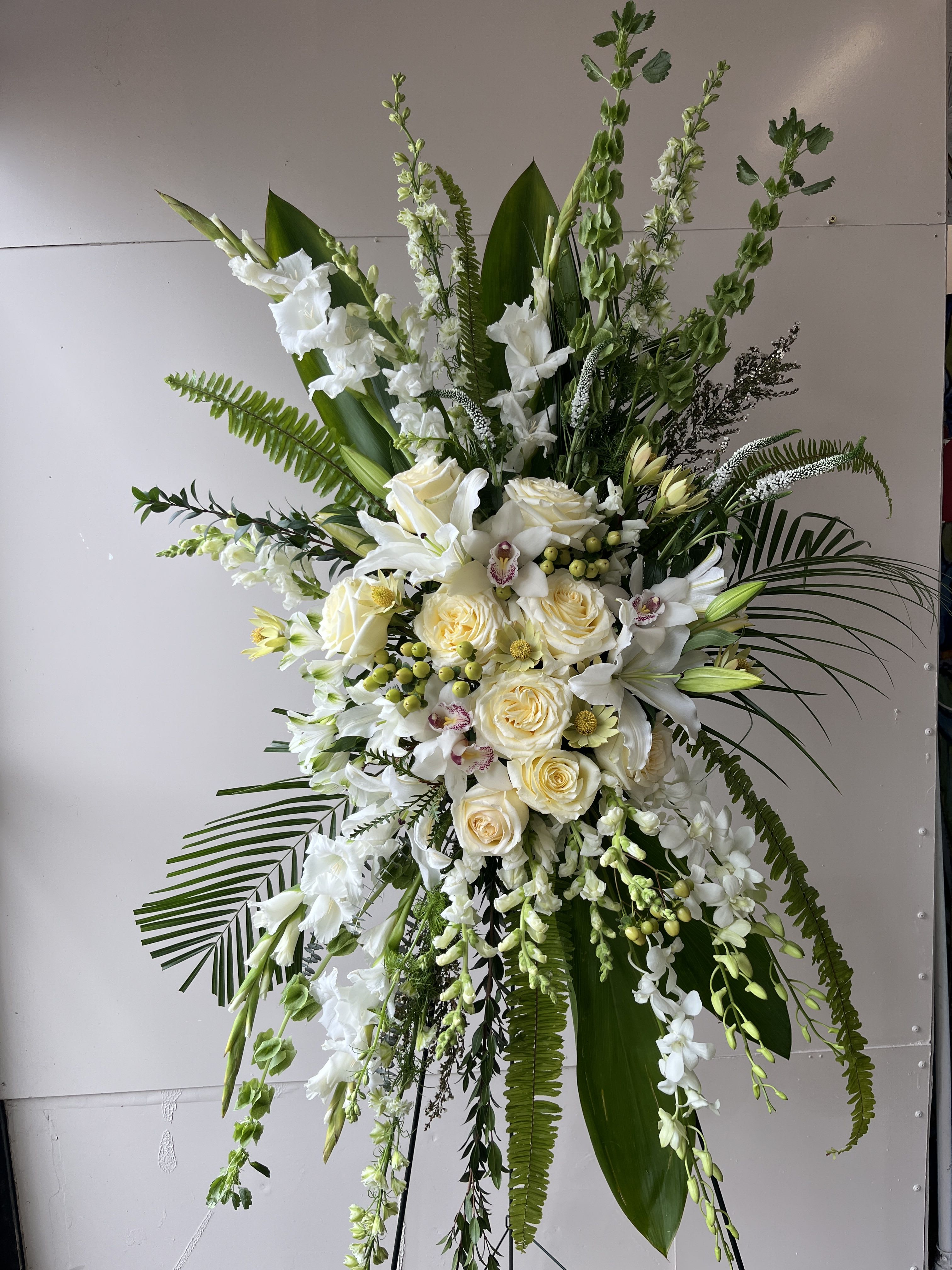 Heaven's Embrace Heaven's Embrace - A timeless tribute of peace and purity, Heaven’s Embrace features cascading white orchids, roses, lilies, and gladiolus, accented with lush greenery and delicate tropical leaves. Designed to convey love, remembrance, and grace, this standing arrangement brings comfort and beauty to moments of farewell.