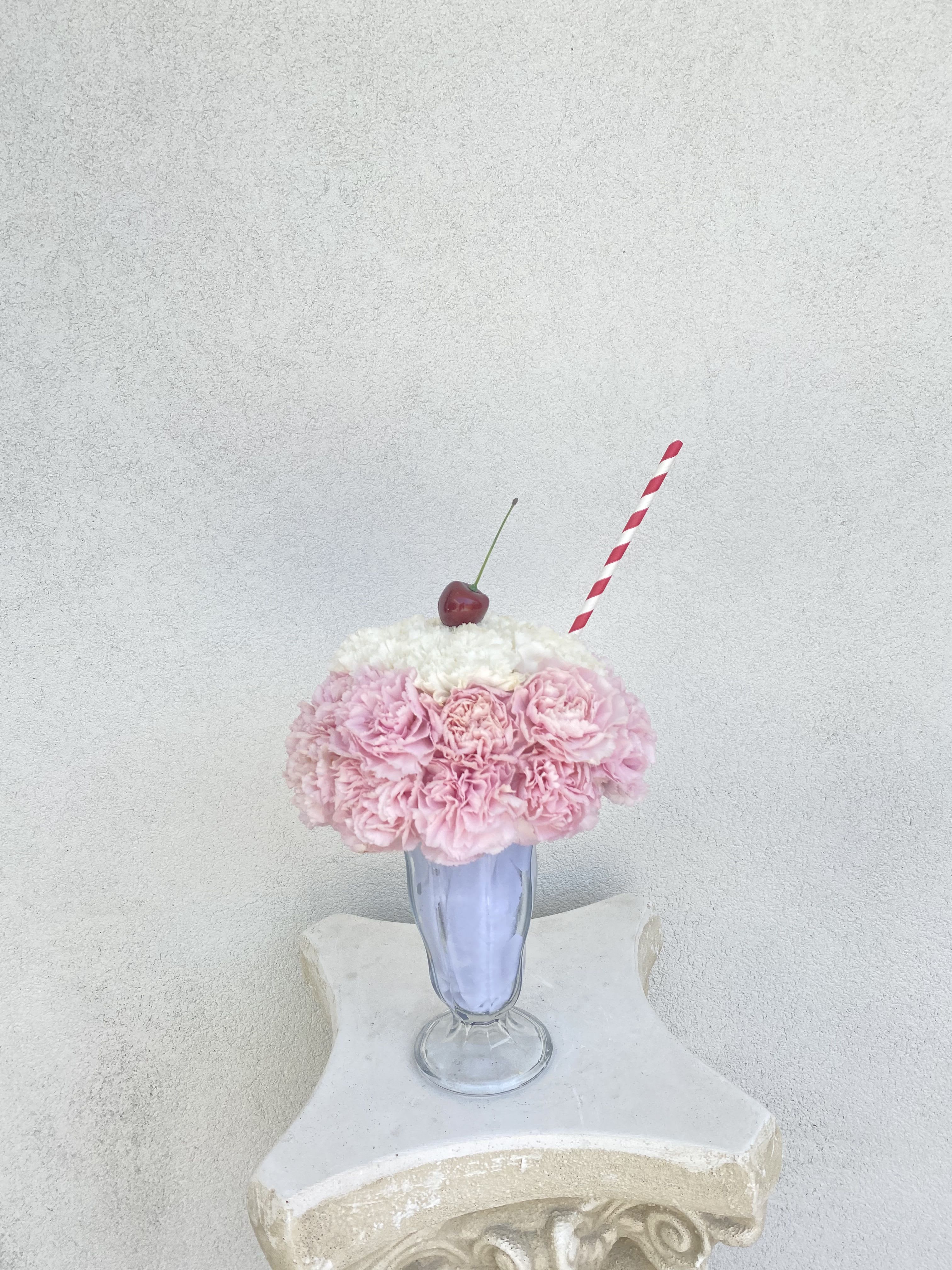 Flower Milkshake Flower Milkshake - It’s always a good time for a milkshake! Pink and White fresh carnations are placed in shape of a delicious milkshake. The perfect gift with a cherry on top! All Sunset Flor arrangements include a flower food package, a care card, and floral info sheet.