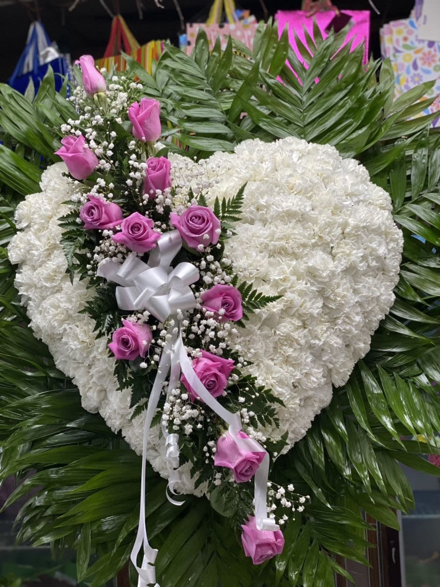 Standing Pure Heart - Send comfort and support with this beautiful heart of white flowers and purple roses perfect for funeral service. We deliver flowers the same day. The heart shaped funeral spray is designed with white carnation and finished with a beautiful arrangement of Lila roses across the center.