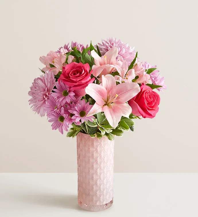 Mother’s Embrace Bouquet - All-around arrangement with hot-pink roses; pink snapdragons, Asiatic lilies, and Peruvian lilies (alstroemerias); and lavender cremons and daisy poms, accented with assorted greenery Artistically designed in a pink glass vase with subtle sparkle and pattern for added finesse; measures 9”H x 4”Dia Extra-large arrangement measures approximately 21” x 14” Large arrangement measures overall approximately 20&quot;H x 12&quot;W Medium arrangement measures overall approximately 19&quot;H x 11&quot;W Small arrangement does not include roses, Asiatic lilies, or snapdragons but does include hot-pink carnations; measures approximately 18&quot;H x 10&quot;W Our florists hand-design each arrangement, so colors, varieties, and container may vary due to local availability To ensure lasting beauty, lilies may arrive in bud form and will fully bloom over the next few days