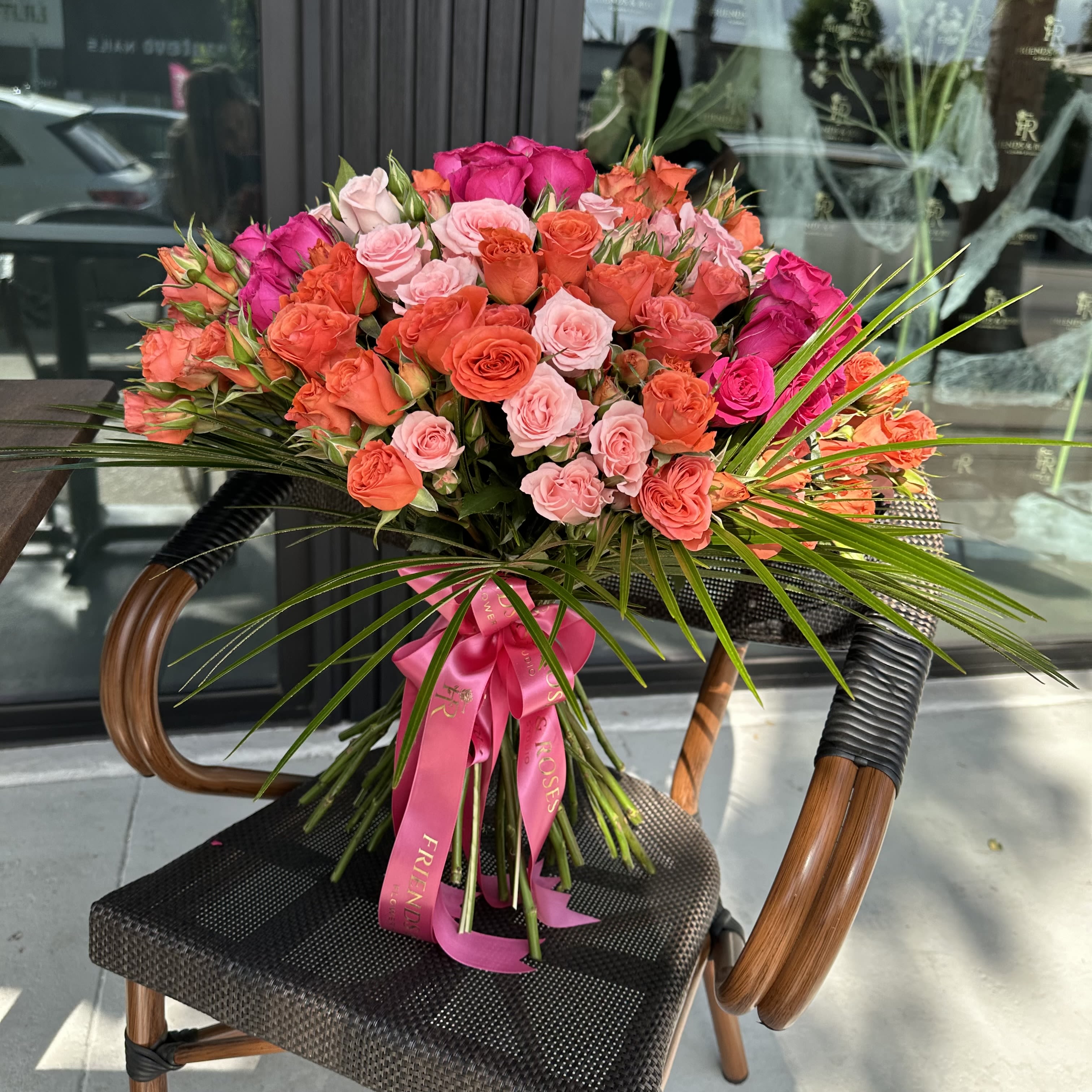 Melody - A vibrant bouquet featuring a stunning mix of orange , delicate pink , and hot pink roses , complemented by lush palm greenery. This cheerful arrangement captures the essence of freshness and energy , making it a perfect choice to brighten any occasion.