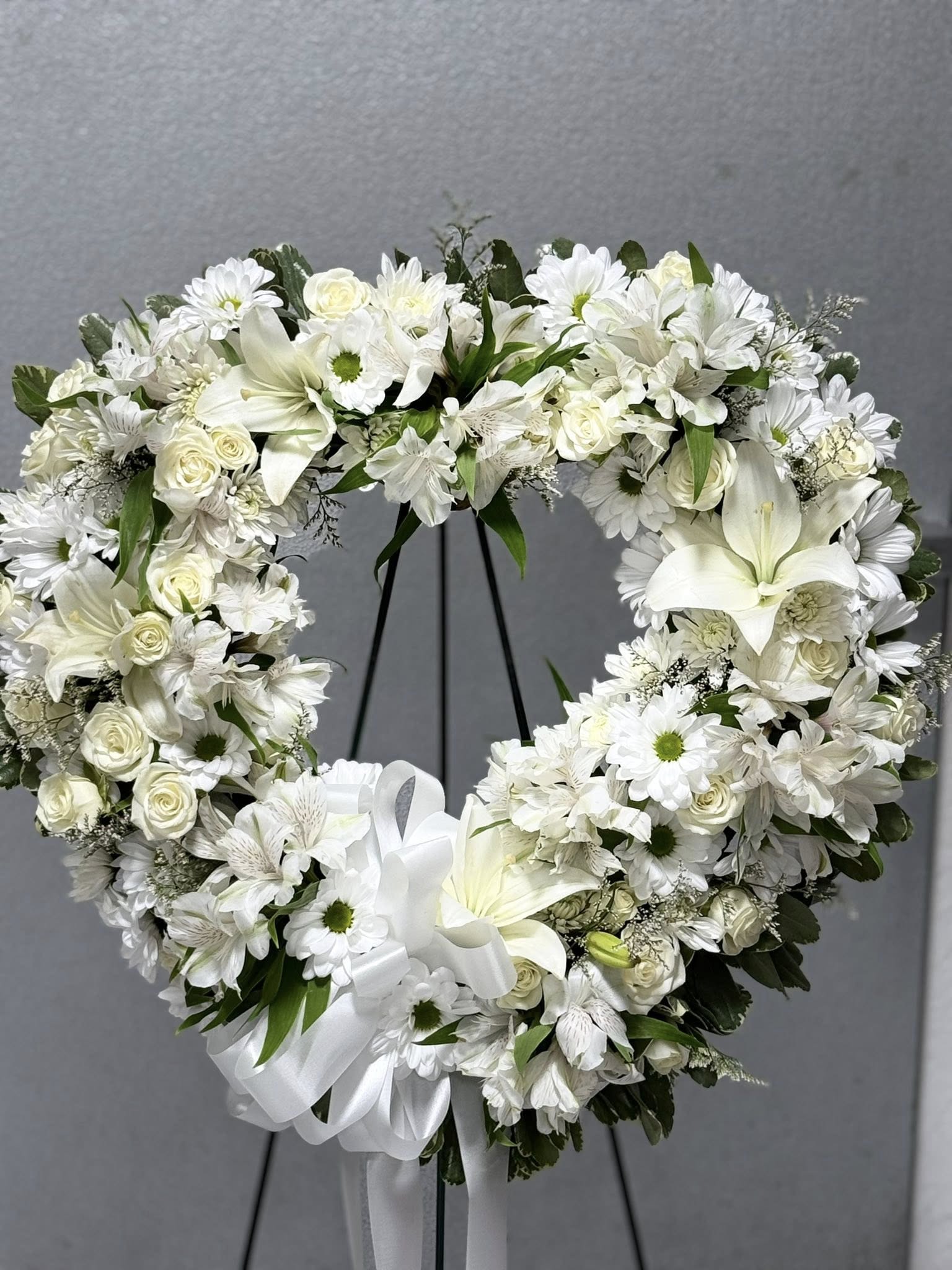 Open Heart Standing Wreath  - Honor a life beautifully lived with our Open Heart Standing Wreath. Designed with care and crafted with fresh, premium blooms, this elegant tribute conveys deep love, sympathy, and remembrance. The open heart shape symbolizes enduring affection and the lasting impact of a loved one's memory. Perfect for funeral services, memorials, or celebration of life ceremonies, this arrangement offers a heartfelt expression of your support and condolences.