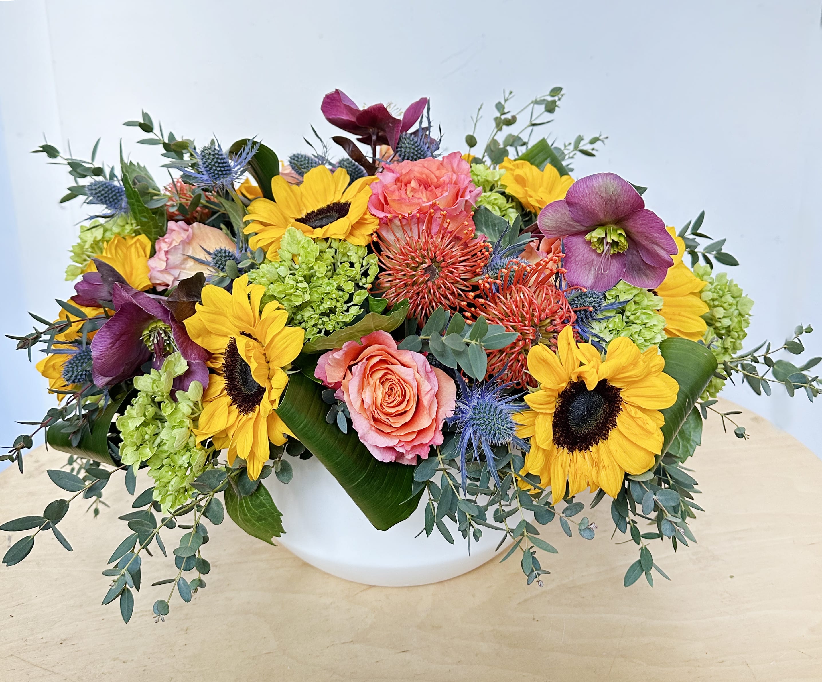 Sunny Side - This arrangement includes sunflowers, green hydrangeas, pincushions, free spirit roses, burgundy hellebore and assorted greens. The arrangement is presented in a very modern white ceramic container. 