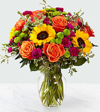 Color Craze - This  blooms with a vibrant energy to create a special moment for your recipient! Our floral professionals weave together a blend of orange roses, sunflowers, violet mini carnations, green button poms, and lush greens to create an incredible gift. Presented in a clear glass vase, this truly colorful display of fresh flowers is ready to send your warmest birthday, thank you, or get well wishes straight to their door.