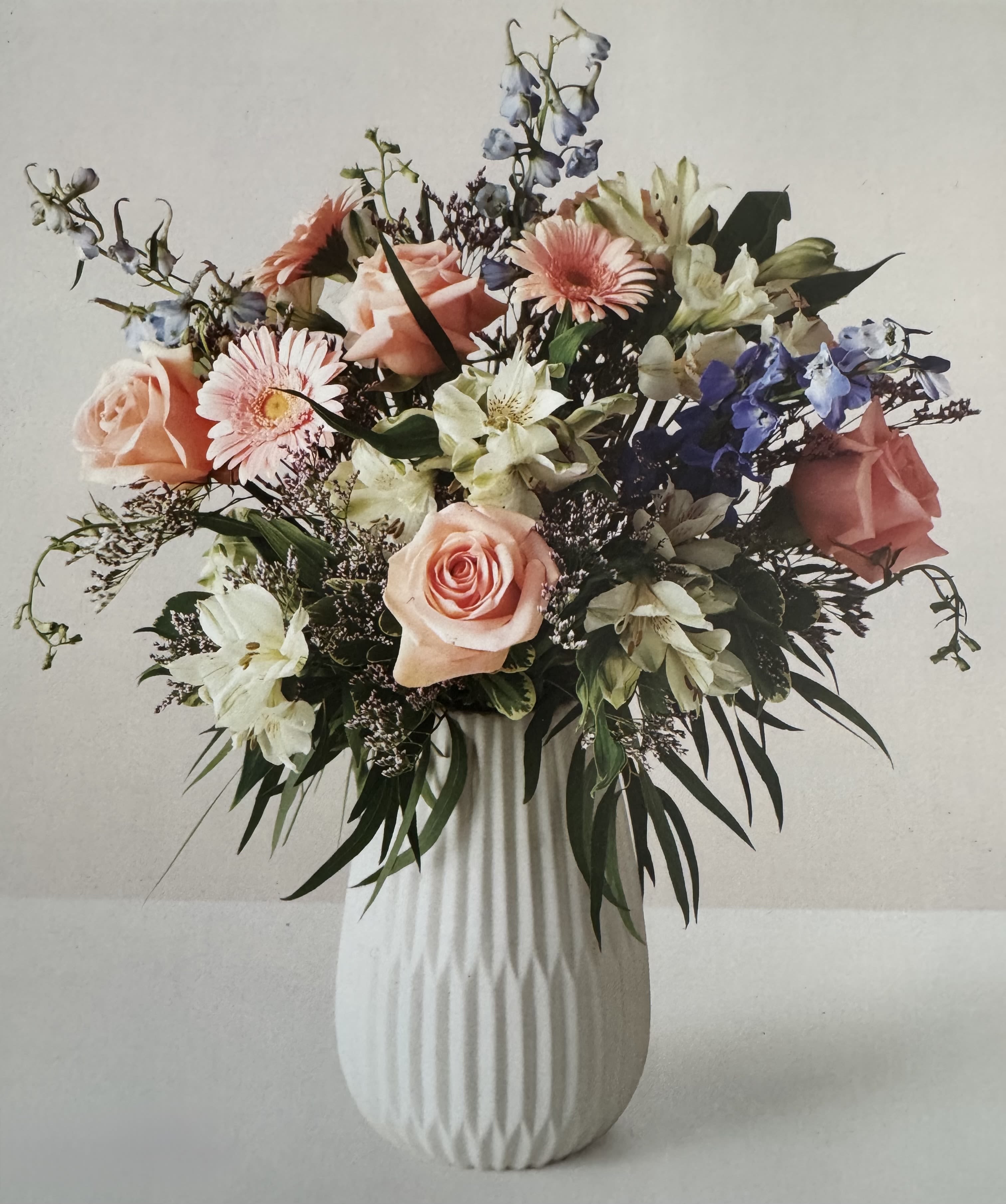 Fields of Beauty Fields of Beauty - A colorful collection of light colored florals arranged in a white clay vase. Colors of florals may vary depending on availability, picture of arrangement displayed is for premium price