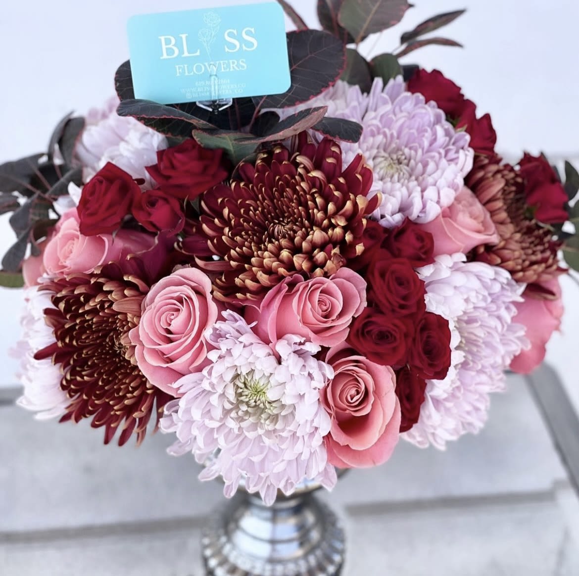 Romance is in the Air Romance is in the Air - This fall favorite includes China mums, spray roses, and freshest reds that is a beautiful varietal.