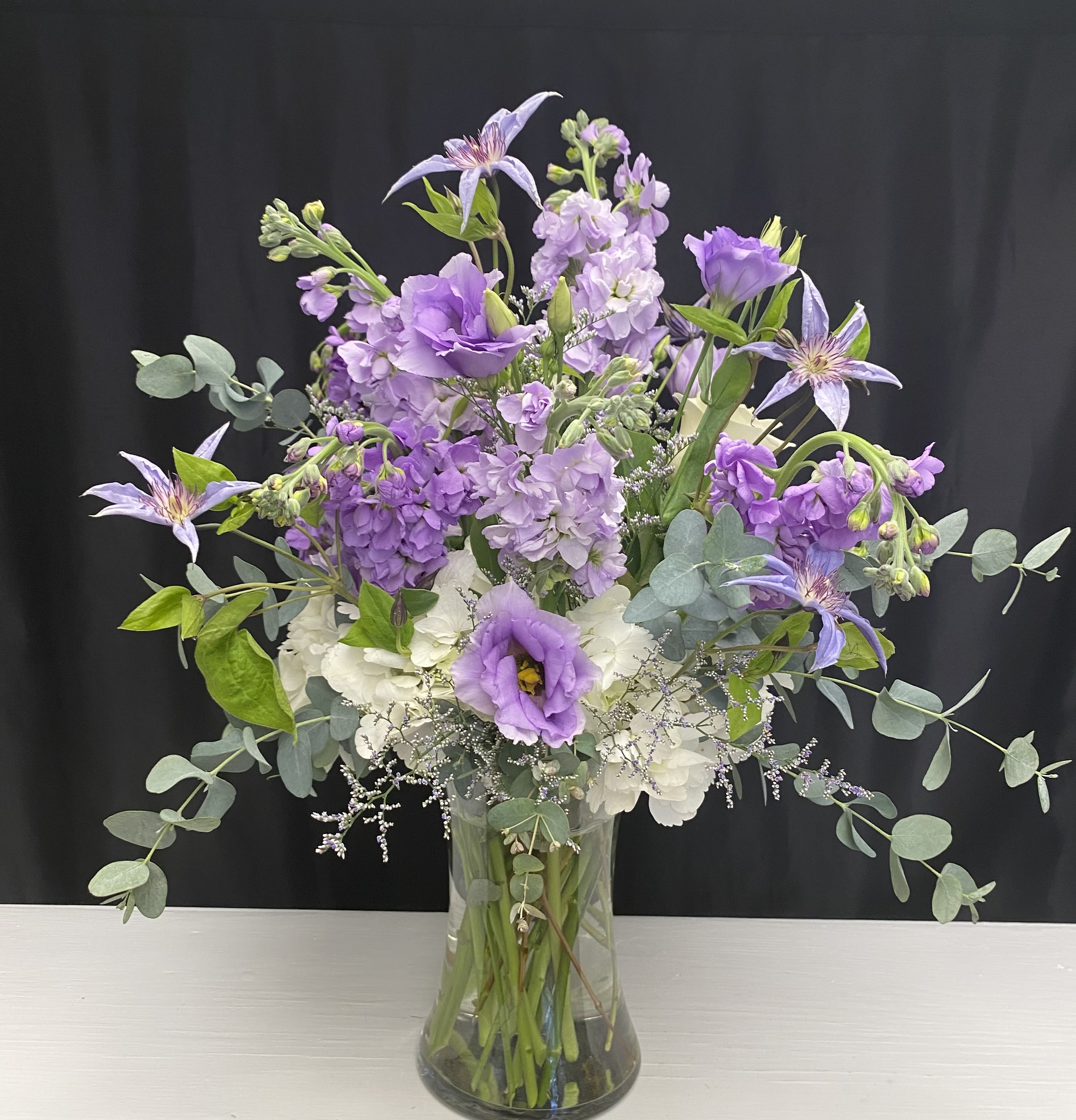 Lush lavenders Lush lavenders - A tall assortment of lavender blooms arranged softly with greenery and sea lavender in a clear vase.