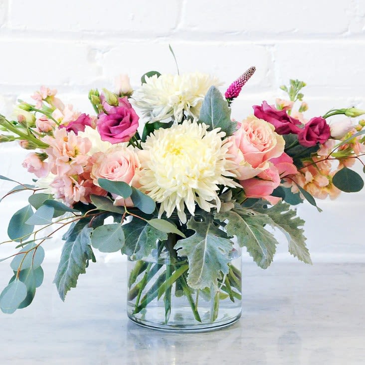Amy - One of our most popular designs, this soft design is full of fragrant pink roses, scented stock and poufs of white standard mums. Available in a glass cylinder.
