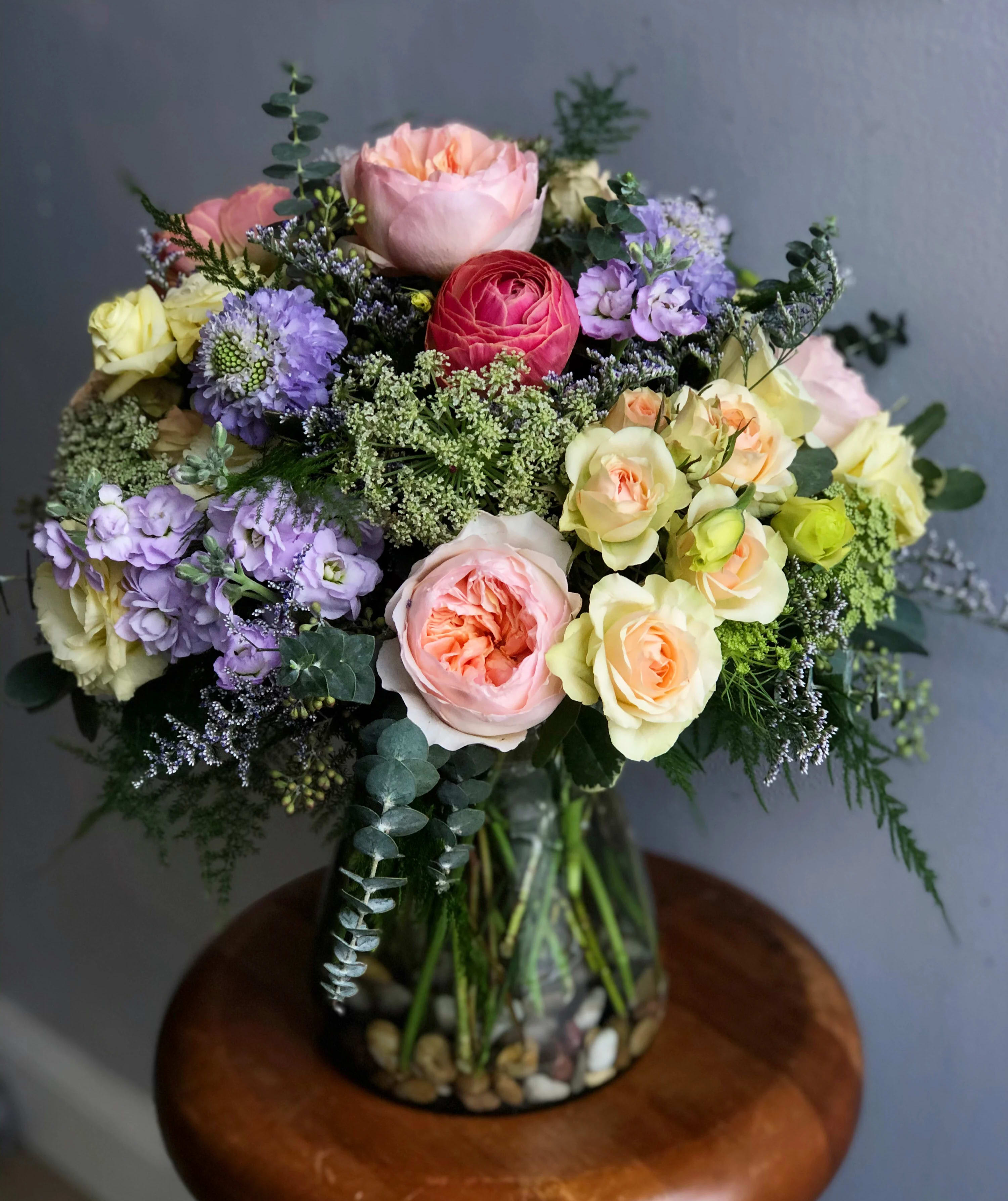 The Madeline by Simply Fresh Flowers - The Madeline is an exquisite &amp; lush, all sided design, of our finest blooms including Juliet garden roses, clooney ranunculus, scabiosa, lisianthus, spray stock, spray roses &amp; green mist, designed within a bed of gorgeous greens &amp; accent blooms.  She is truly a premium arrangement meant for someone incredibly special. Simply a showstopper!